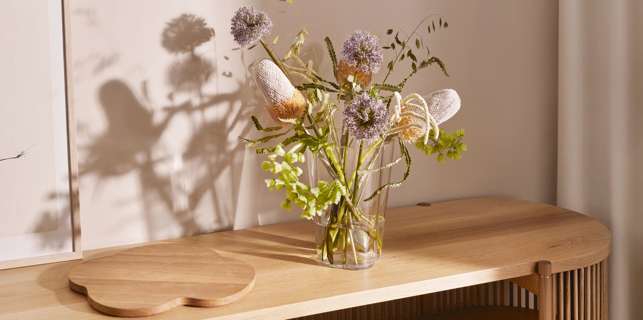 Konsolbord i ljust trä med en hjärtformad skiva, en vas med gröna växter och en marmorskiva med ett mörkt föremål.