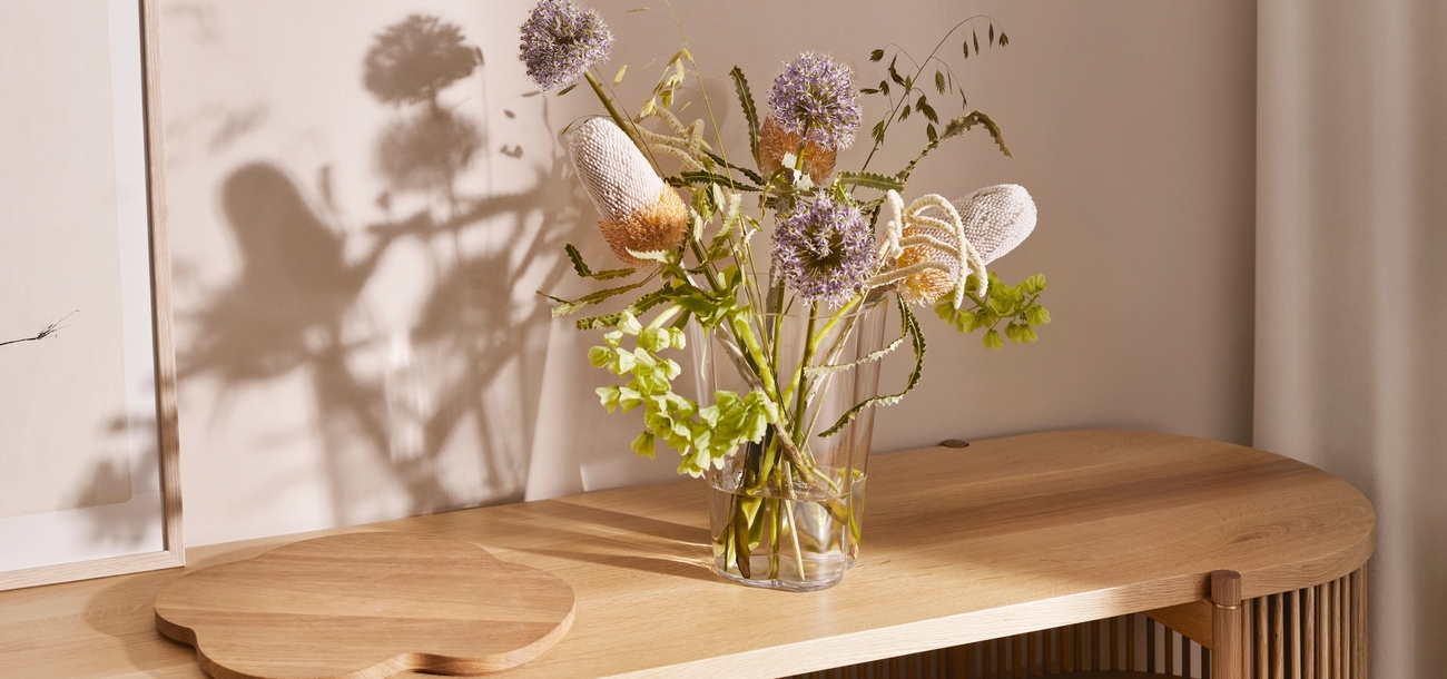 Konsolbord i ljust trä med en hjärtformad skiva, en vas med gröna växter och en marmorskiva med ett mörkt föremål.