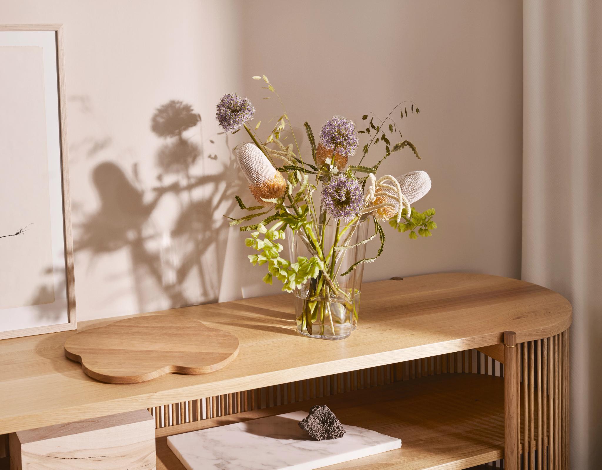 En vas med våriga blommor står på en träbänk i ett vardagsrum