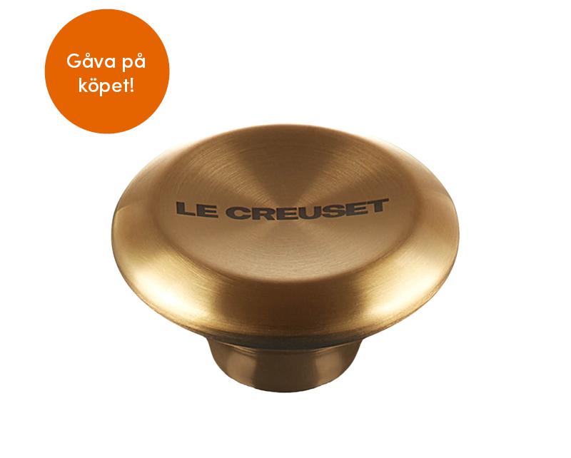 En guldknopp från Le Creuset på vit bakgrund