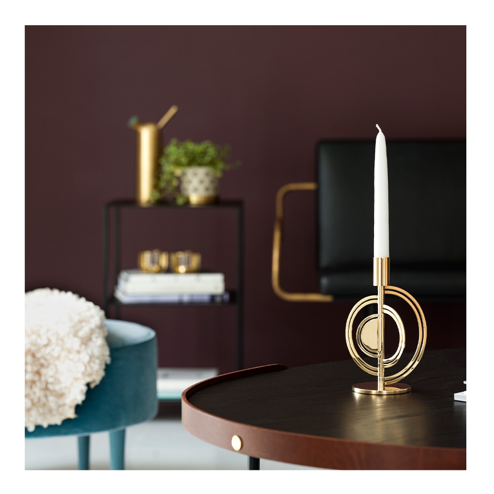 Gold candle holder with a white candle on a dark wood table.
