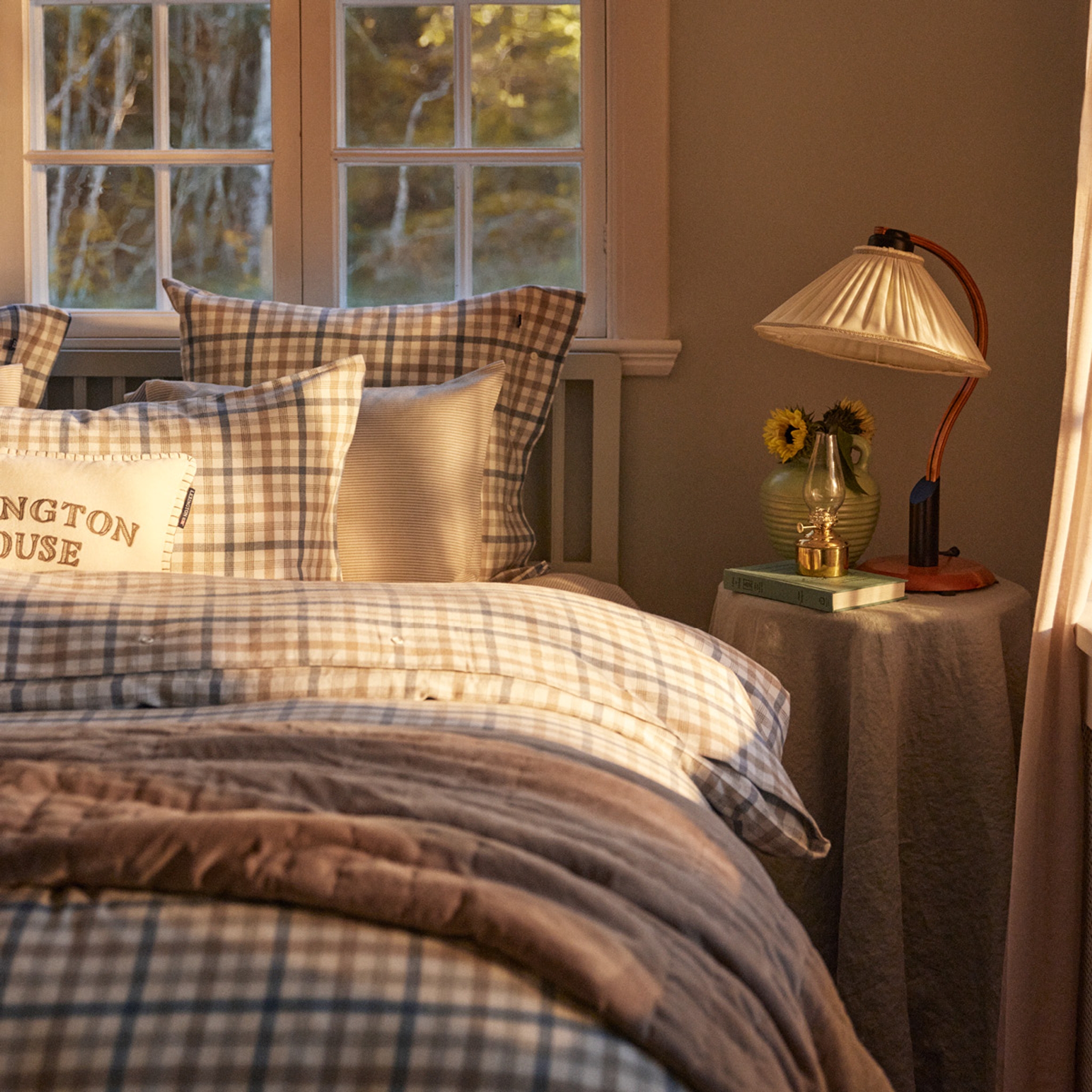 Ett sovrum i kvällsljus med en säng bäddad med rutiga lakan