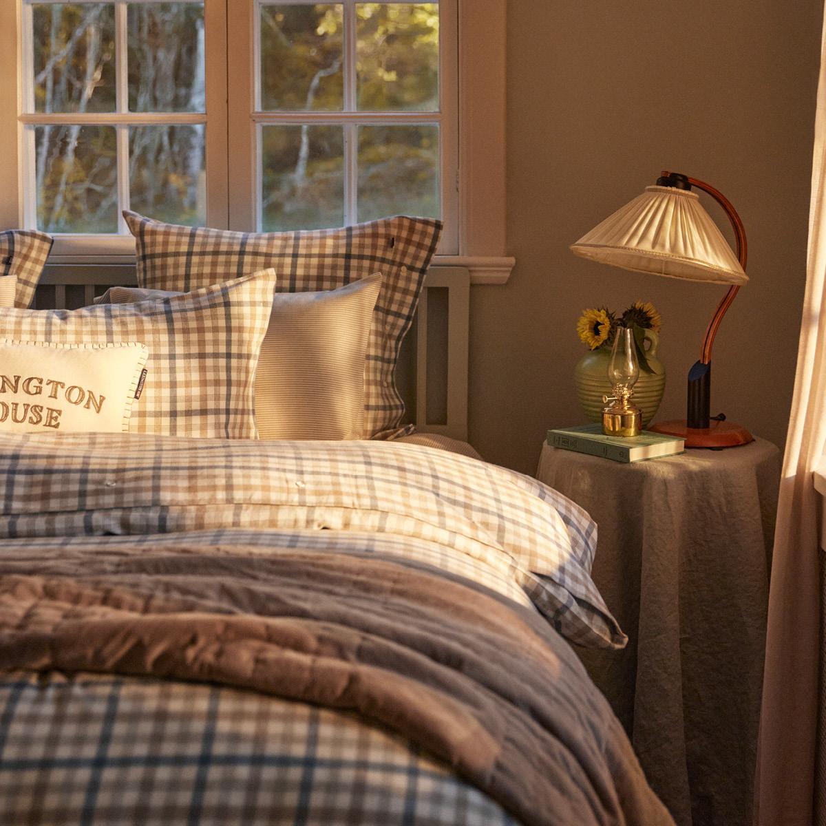 Ett sovrum i kvällsljus med en säng bäddad med rutiga lakan