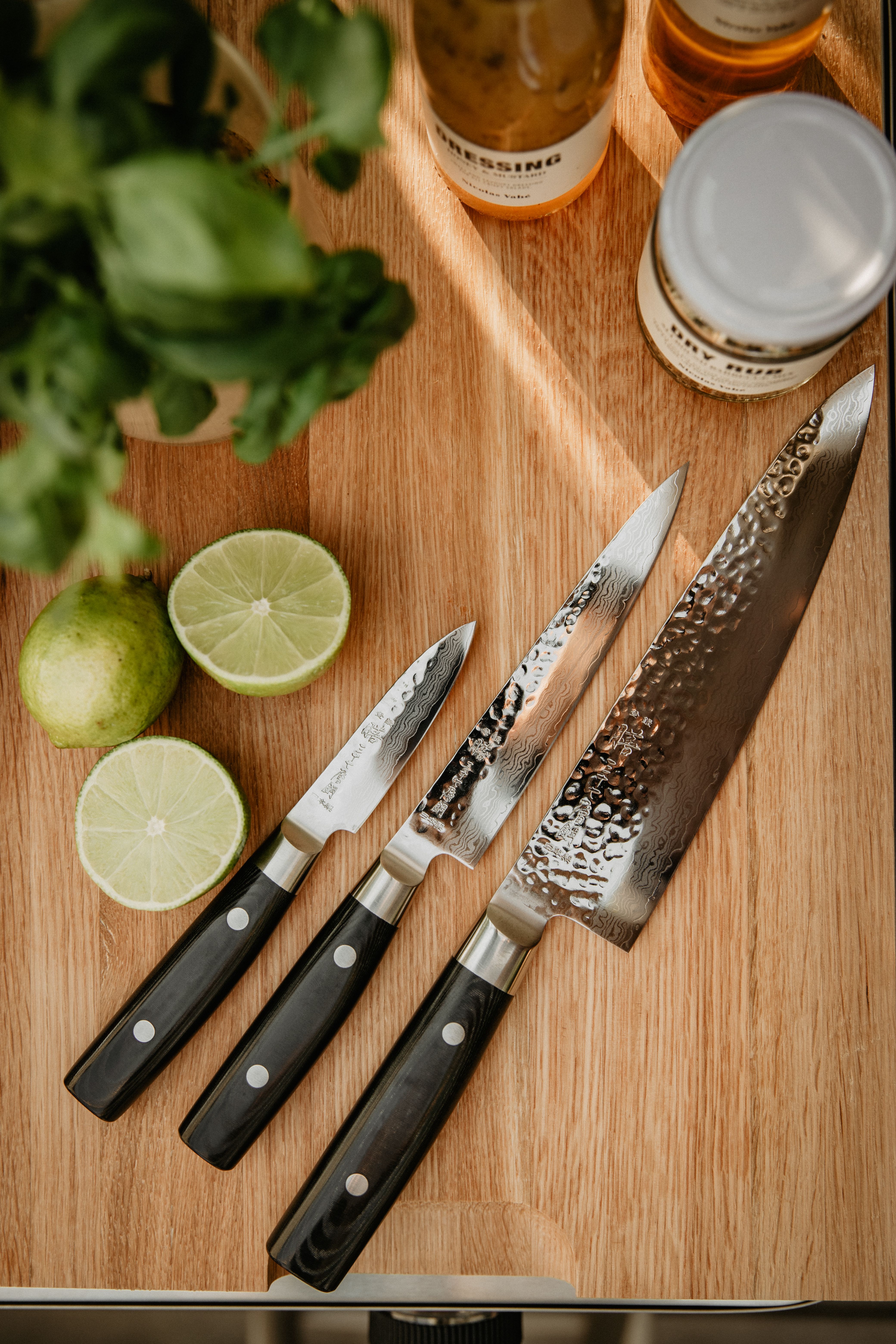 Tre kniver ligger på et skjærebrett av tre med en lime ved siden av