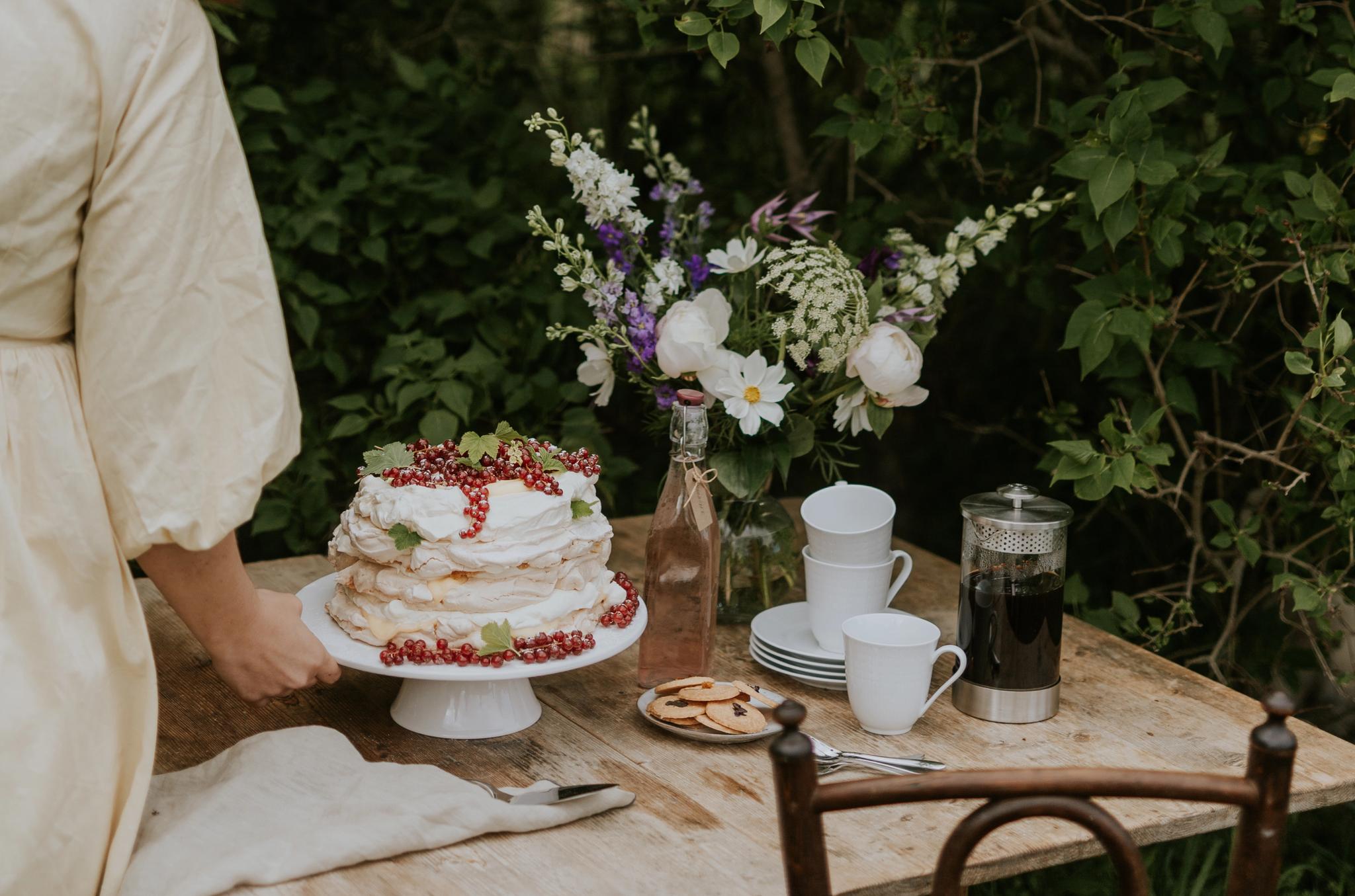 Somrig trädgårdsfika med tårta, kaffe och blommor på ett rustikt träbord.
