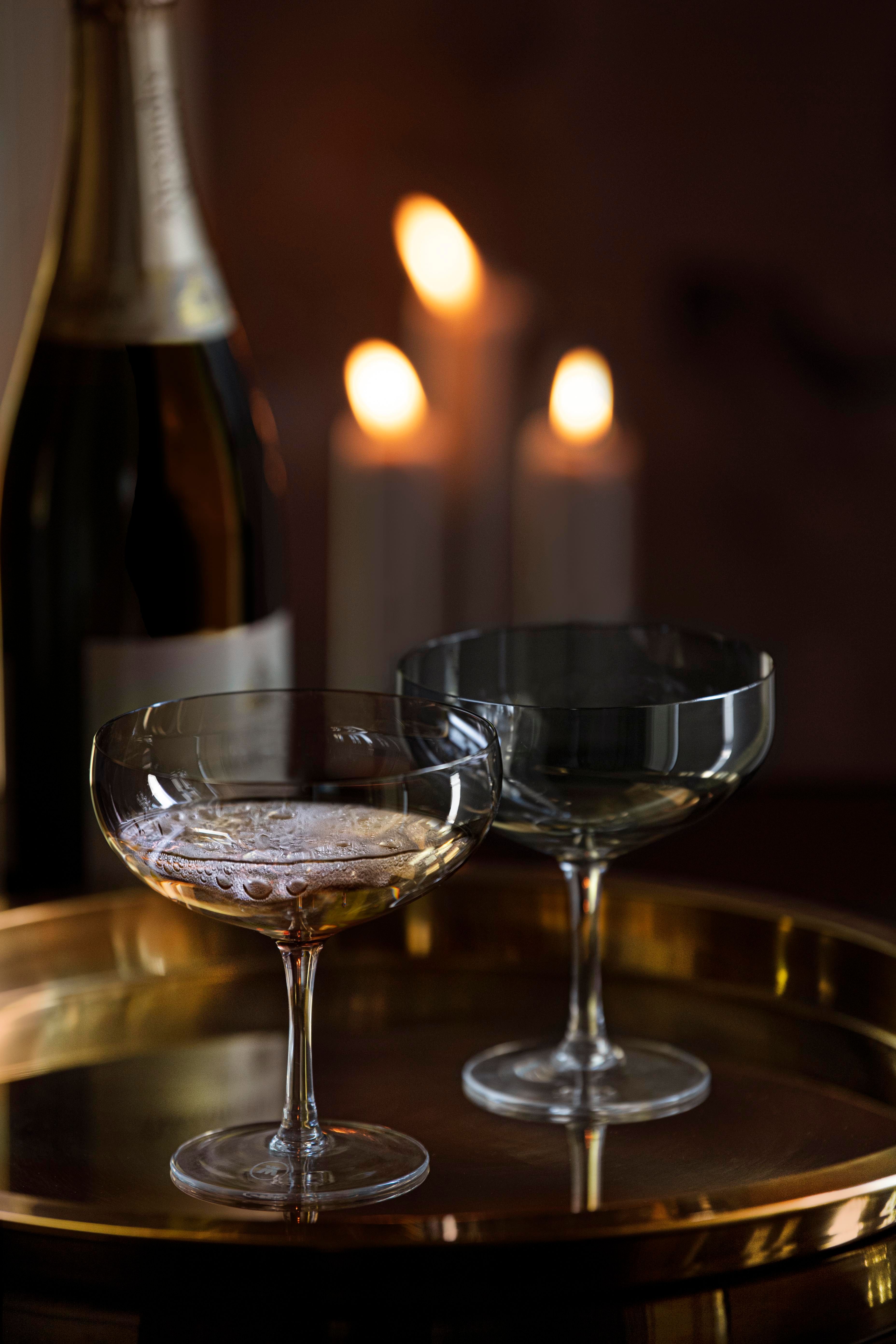 Champagneflaske og to coupeglass på et gyllent brett foran levende lys.