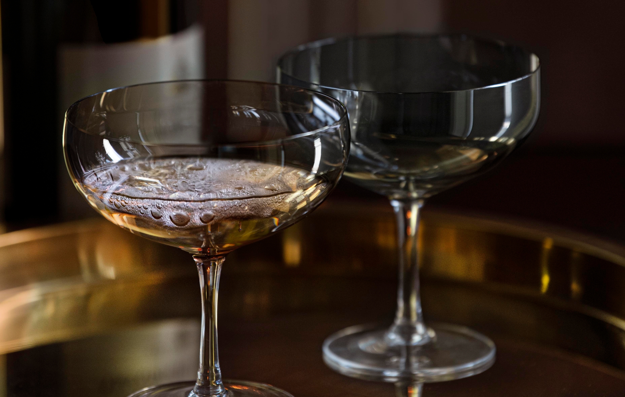 Champagneflaske og to coupeglass på et gyllent brett foran levende lys.