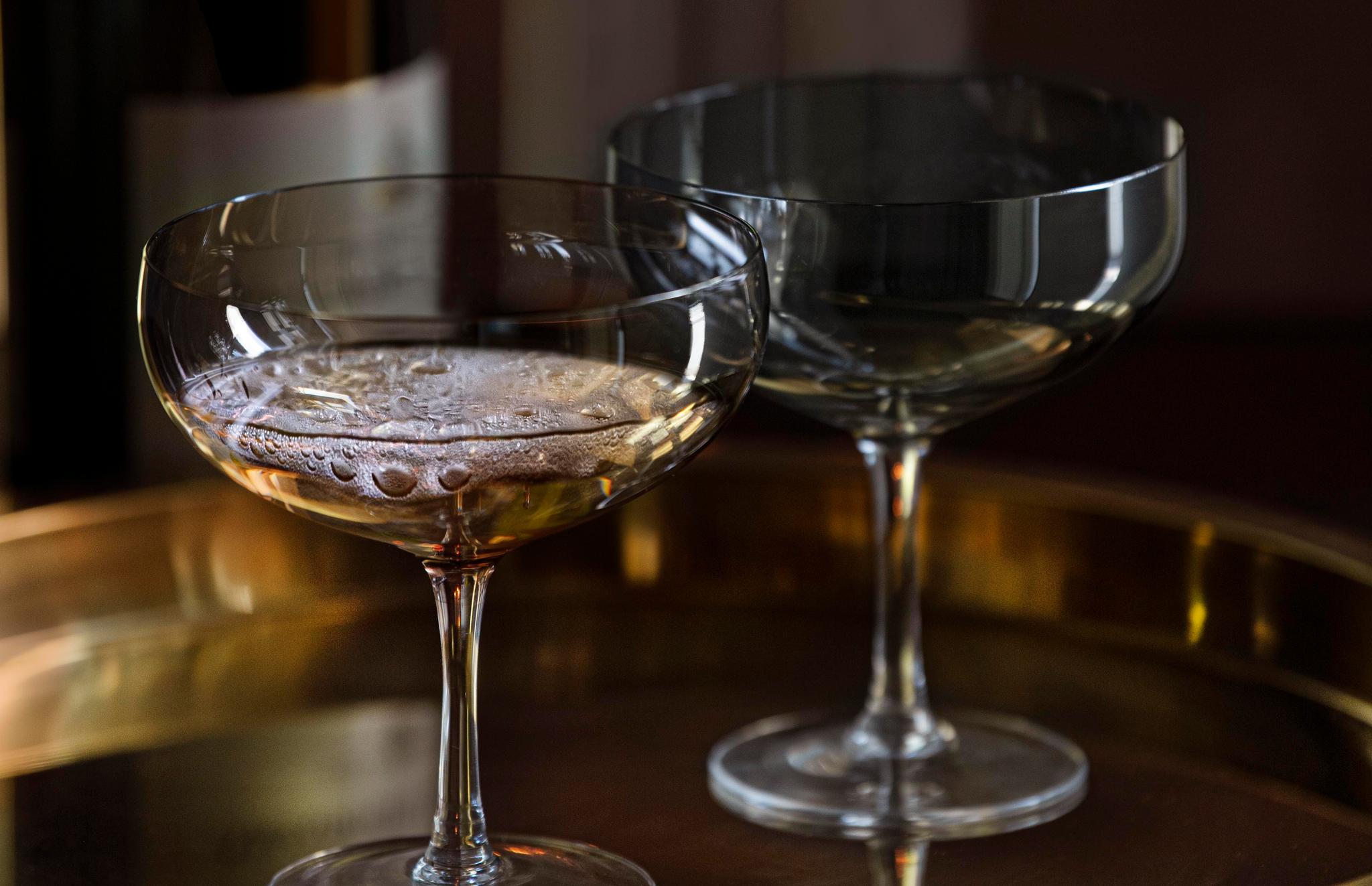 Champagneflaske og to coupeglass på et gyllent brett foran levende lys.