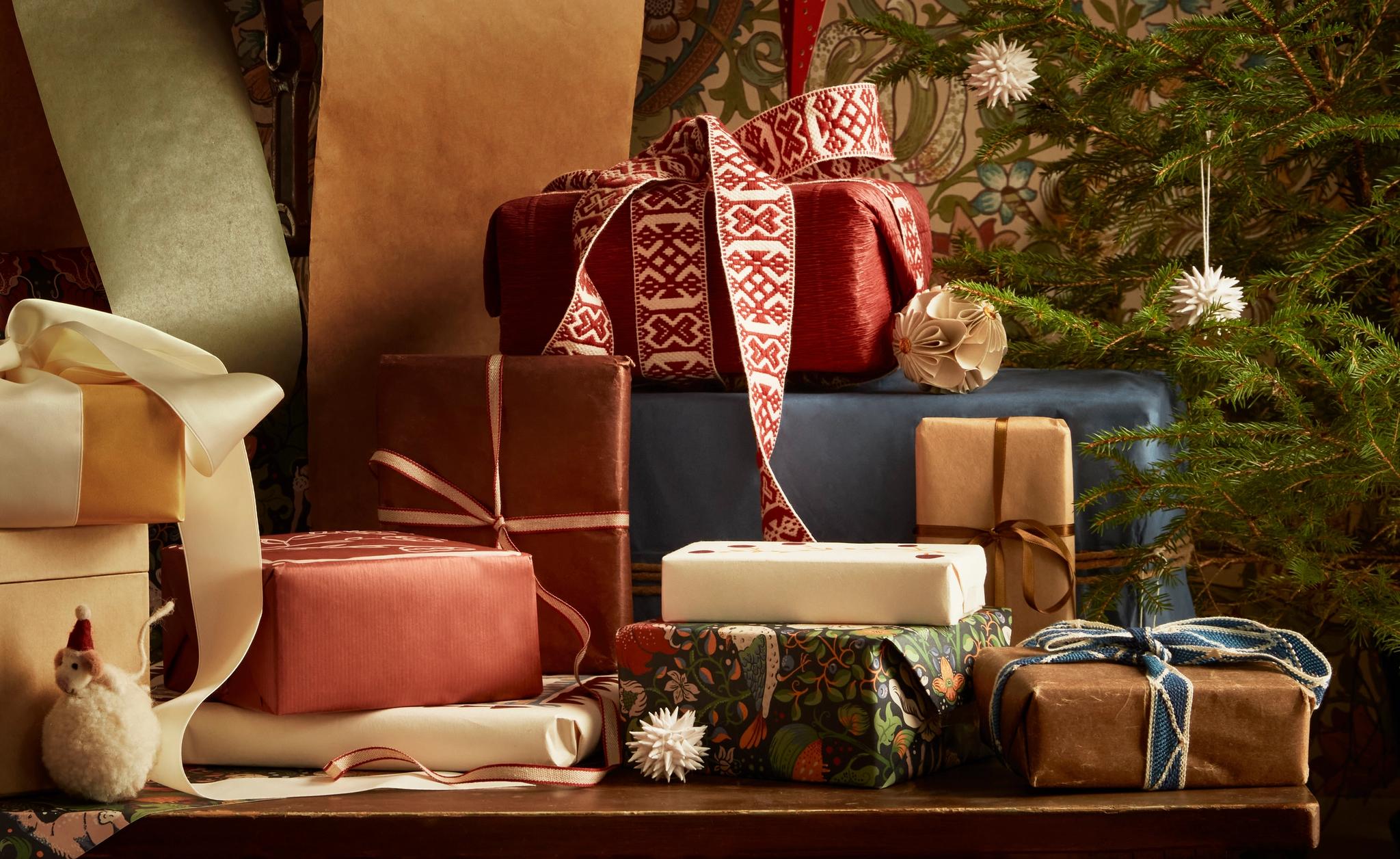 A collection of wrapped Christmas gifts in various papers and ribbons, next to a small decorated Christmas tree.