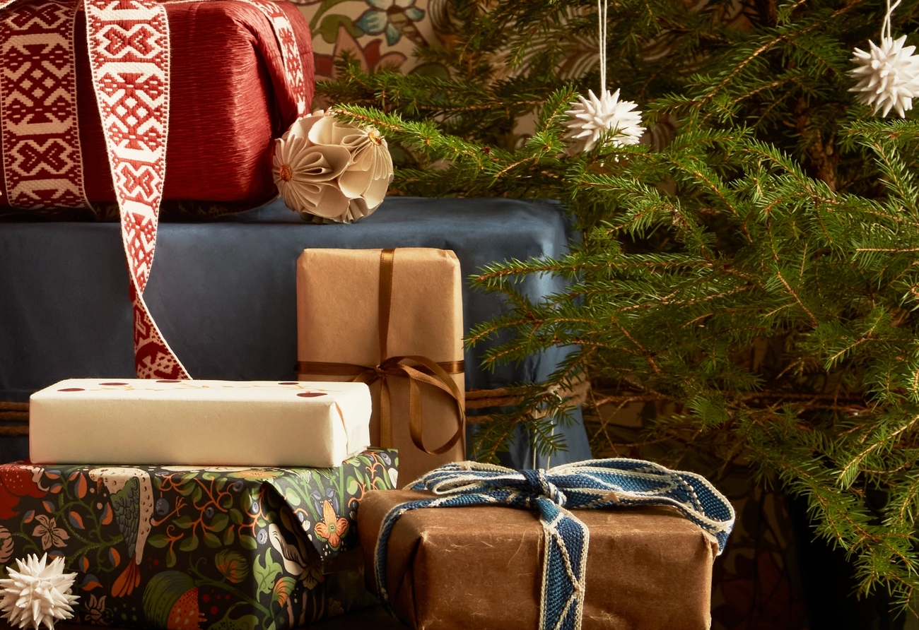 A festive display of wrapped Christmas presents in various papers and ribbons, next to a small decorated tree.