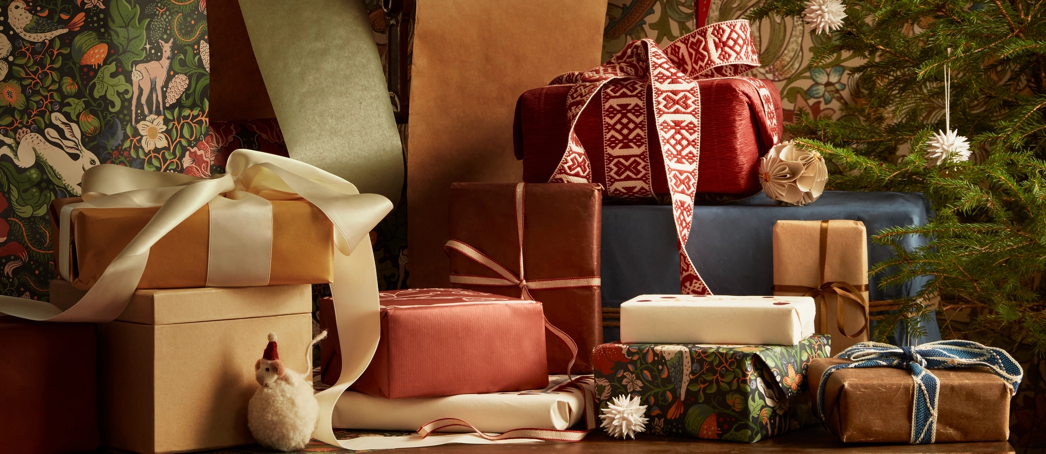 A festive display of wrapped Christmas gifts, some with decorative ribbons, next to a small decorated Christmas tree.