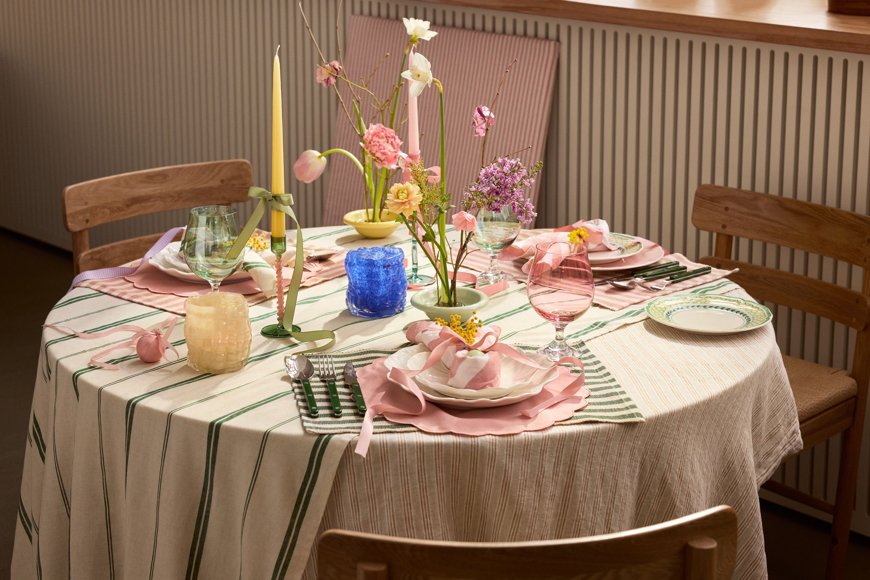 Dukning till påsk på grönrandig duk med vita tallrikar och rosa servetter