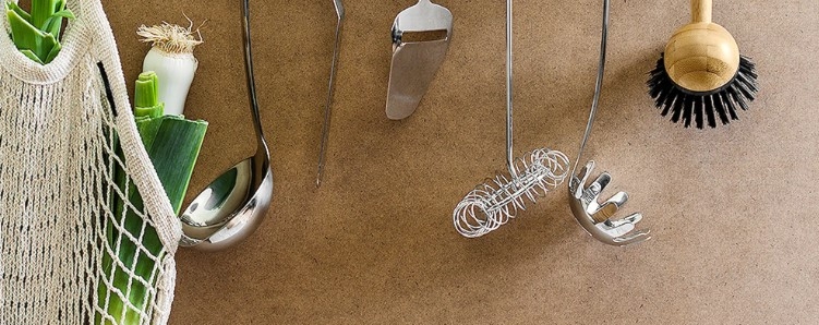 Grytredskaper & Sleiver hengende mot brun bakgrunn samt et hvitt heklet handlenett med purreløk