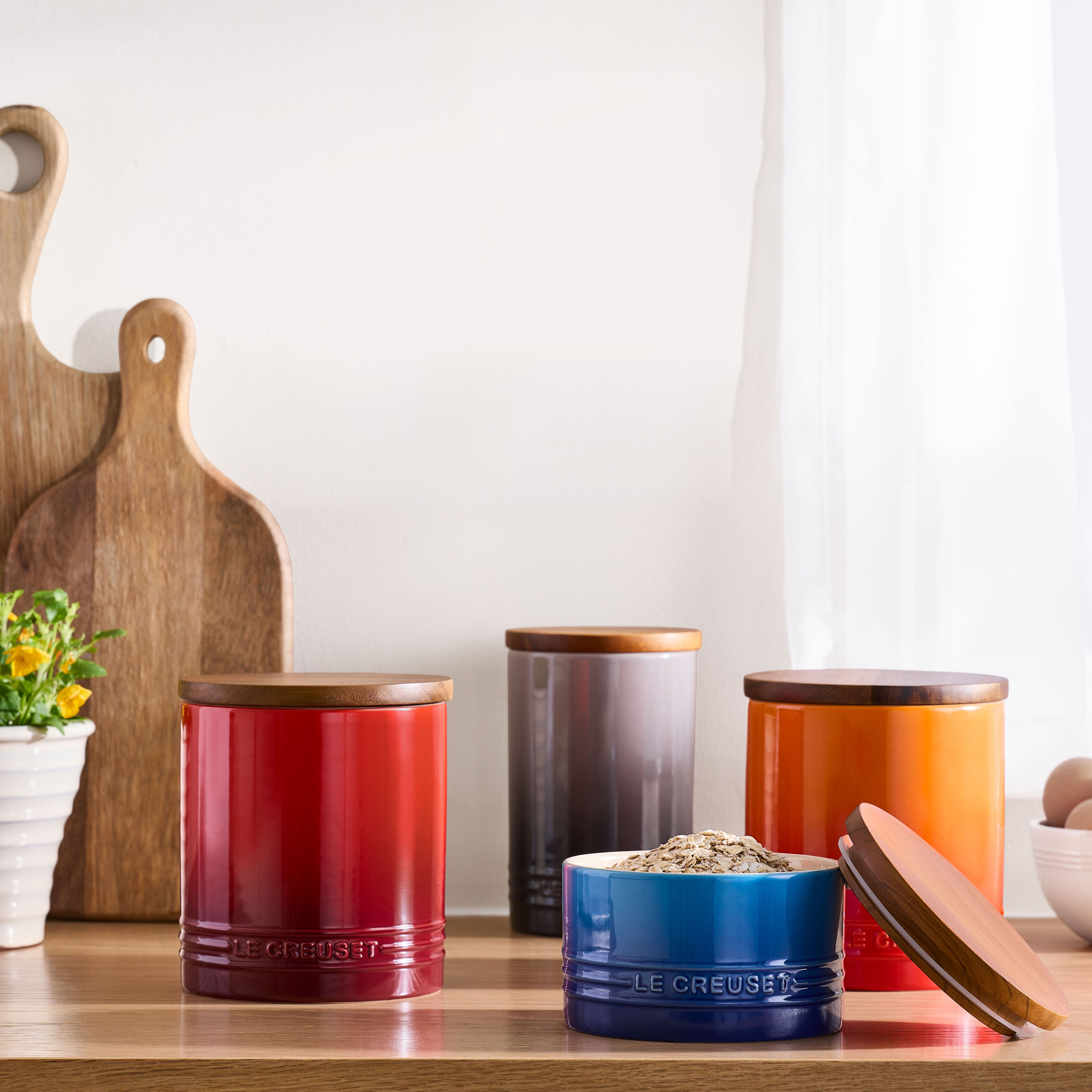 Färgglada Le Creuset-förvaringsburkar med trälock står på en köksbänk tillsammans med skärbrädor och blommor.