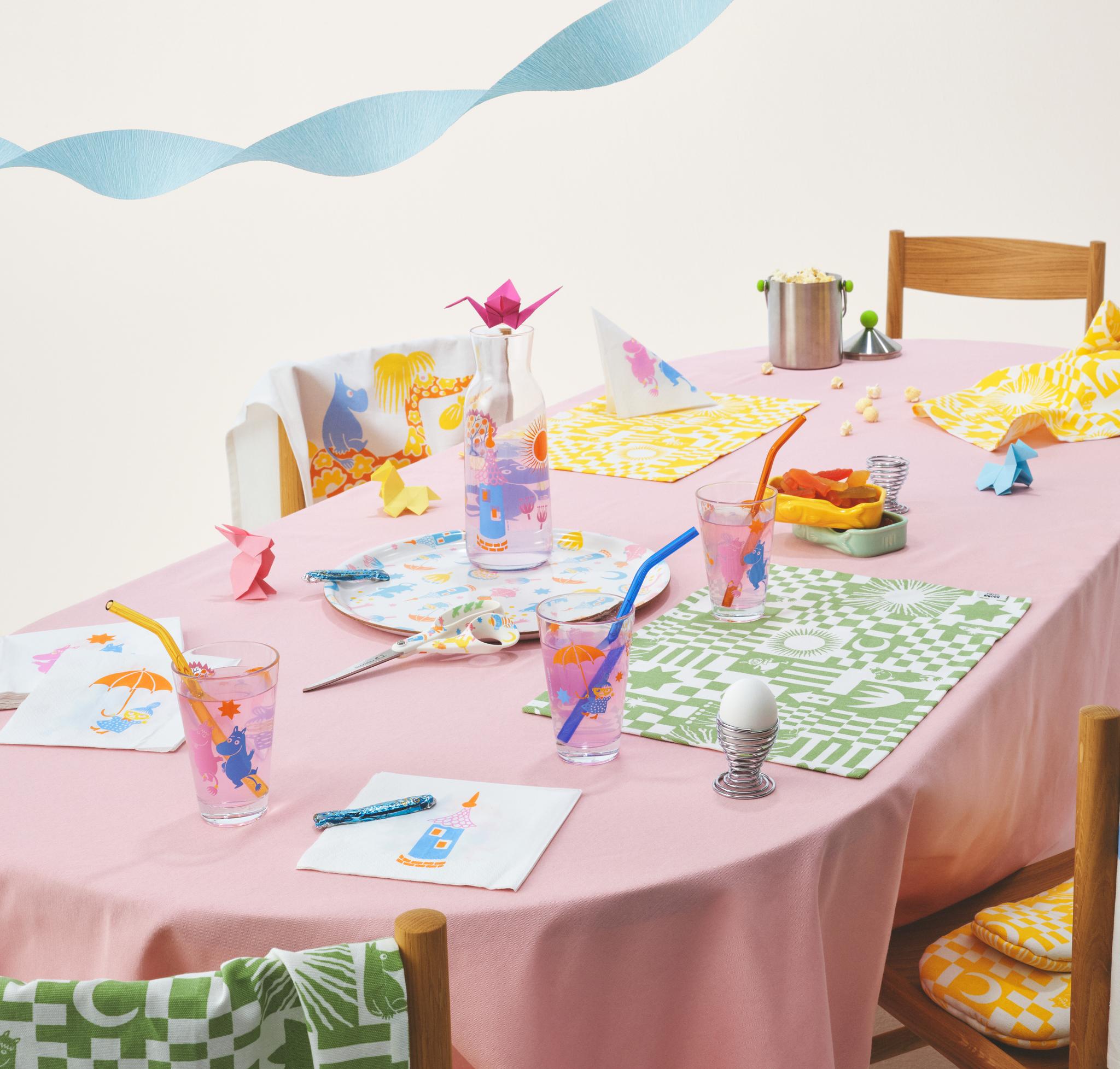 Muumi juhlat kokoelma katetulla pöydällä täynnä pastellivärejä, laseja, servettejä, tarjotin ja pöytätabletit