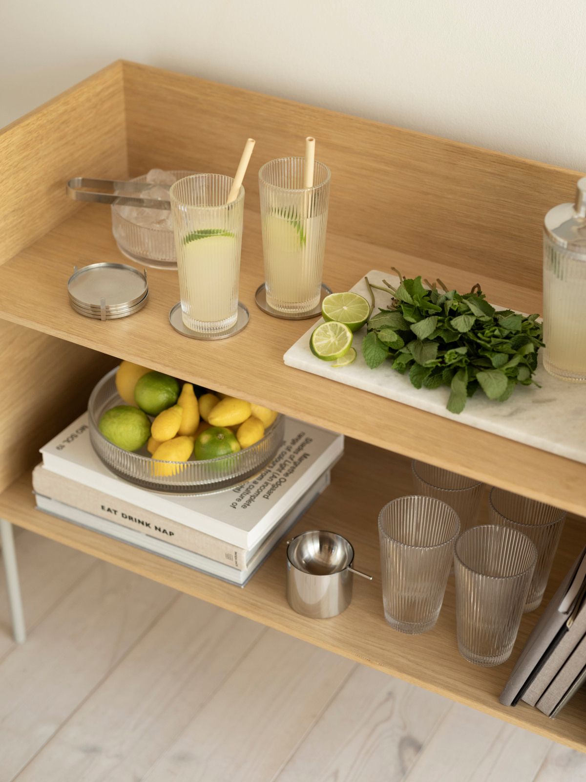 Stilren serveringsvagn i trä med lemonad i höga glas, färska citroner, lime och mynta redo för somrig drinkservering.