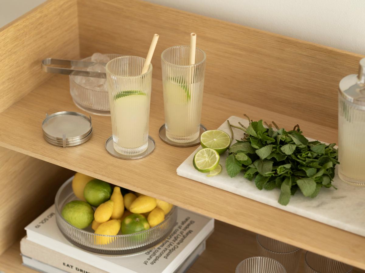 Stilren serveringsvagn i trä med lemonad i höga glas, färska citroner, lime och mynta redo för somrig drinkservering.