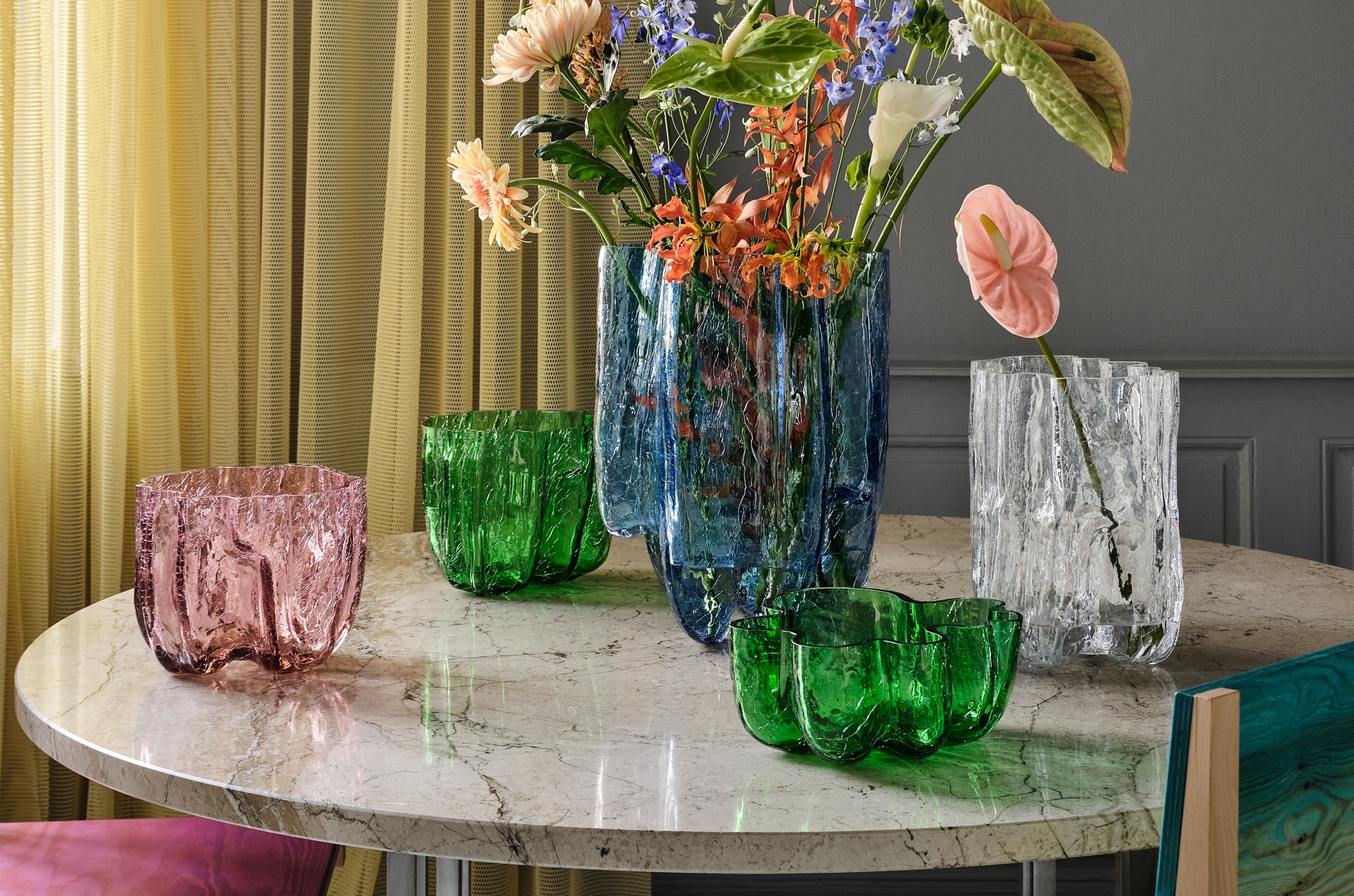 Färgglada, strukturerade glasvaser med blommor står på ett runt marmorbord i ett modernt, stilrent rum.