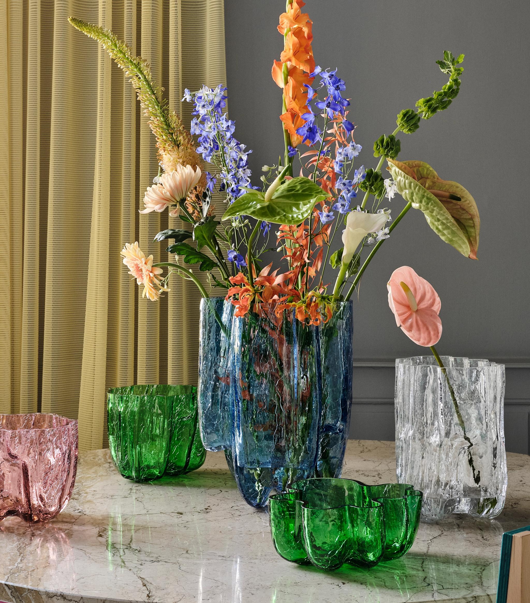 Färgglada glasvaser i olika storlekar och färger står på ett bord.