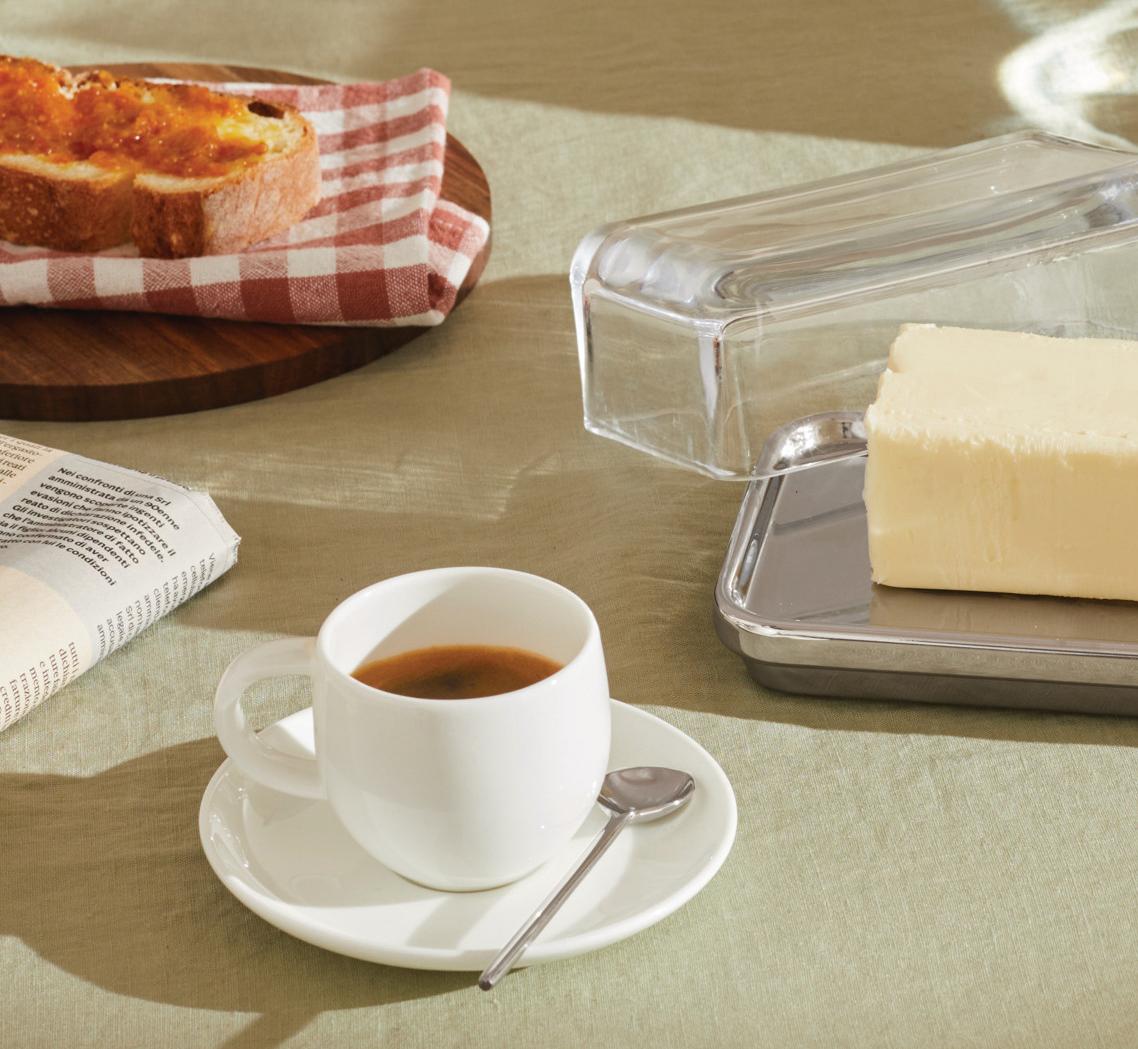 Frukostdukning med smör i smörbytta, en kopp kaffe och rostat bröd på ett bord med grön duk.