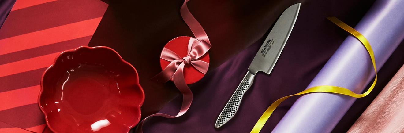 Rød bolle, gaveeske og Global kjøkkenkniv på mønstret papir med bånd.