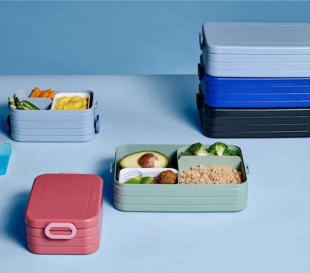 Colorful, stackable lunch boxes, some open with partitioned food and others closed.
