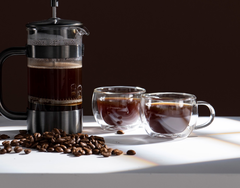 Glasmuggar med kaffe i och en pressobryggare