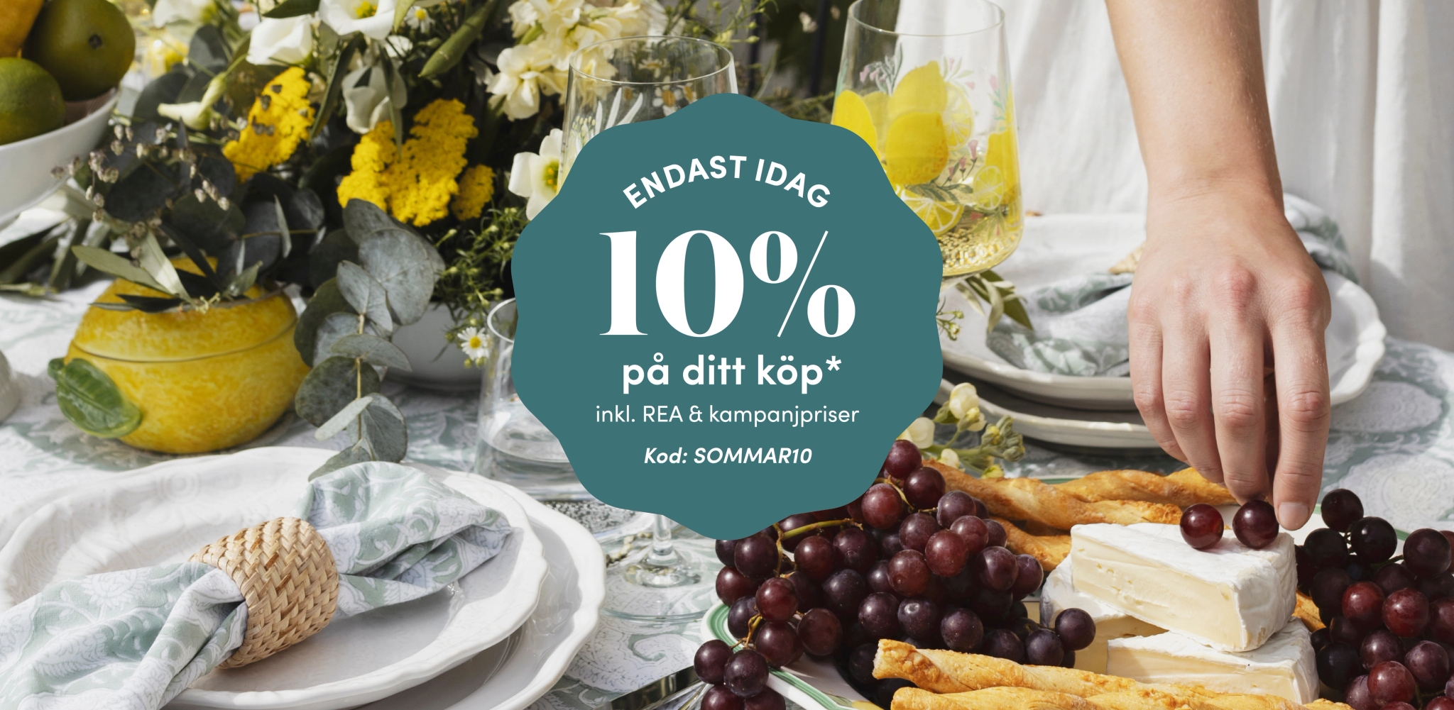 Somrig dukning med ost, vindruvor och blommor samt kampanjtext om 10% rabatt med rabattkod SOMMAR10.