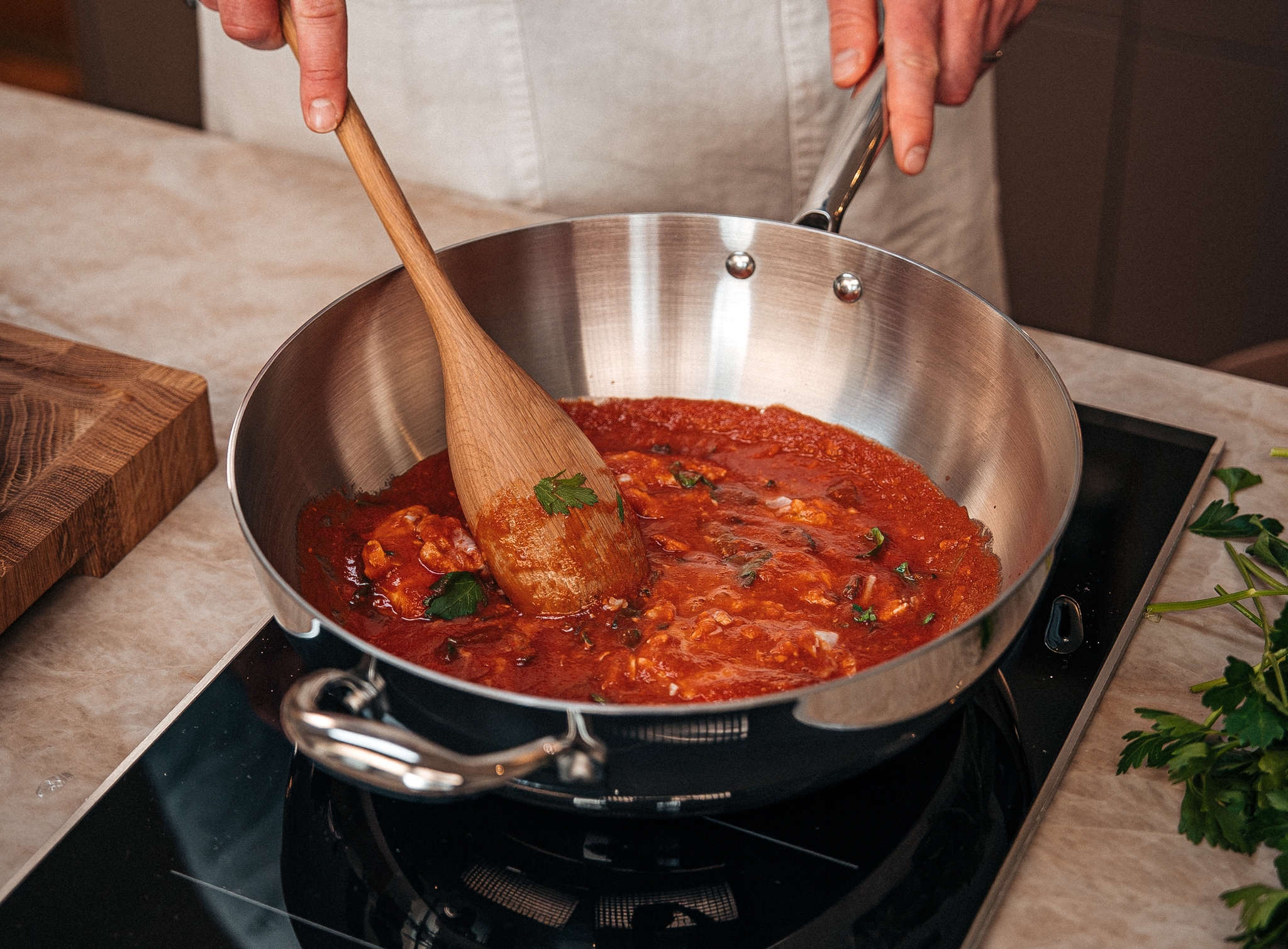 Person som rör om en tomatbaserad pastasås i en stor stekpanna på spisen.
