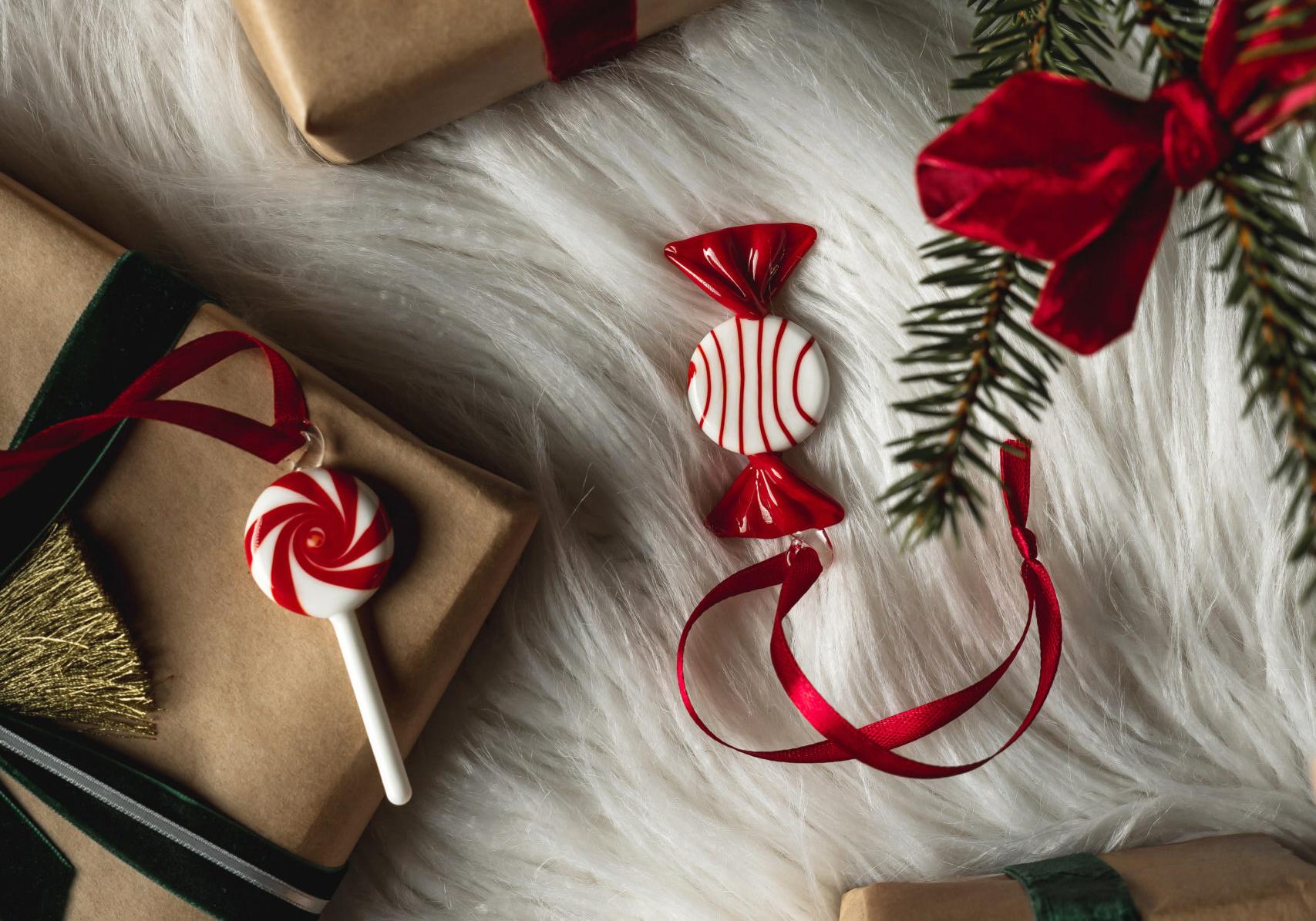 Christmas gifts wrapped in brown paper with red and green velvet ribbons, alongside candy decorations and a pine branch, on white faux fur.