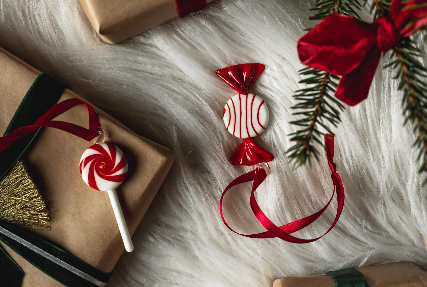 Gaver i brunt papir med røde og grønne fløyelsbånd, godteri pynt og furugrener på hvit fuskepels