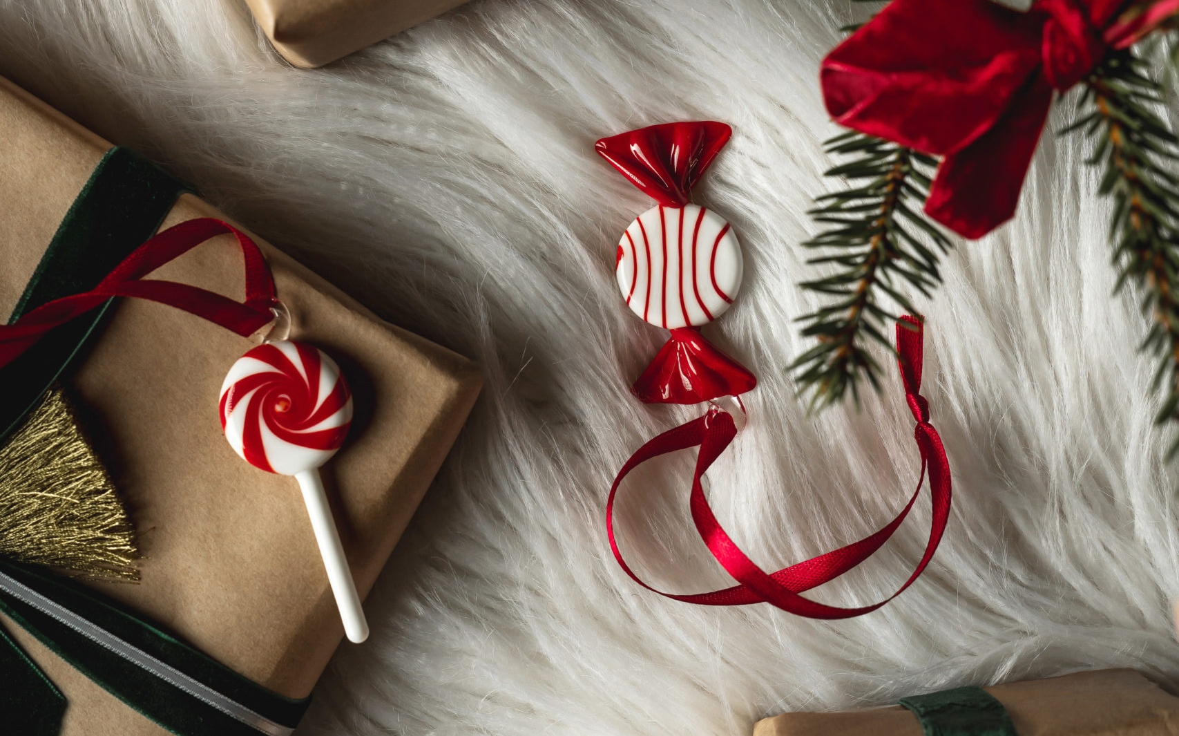 Gaver i brunt papir med røde og grønne fløyelsbånd, godteri pynt og furugrener på hvit fuskepels