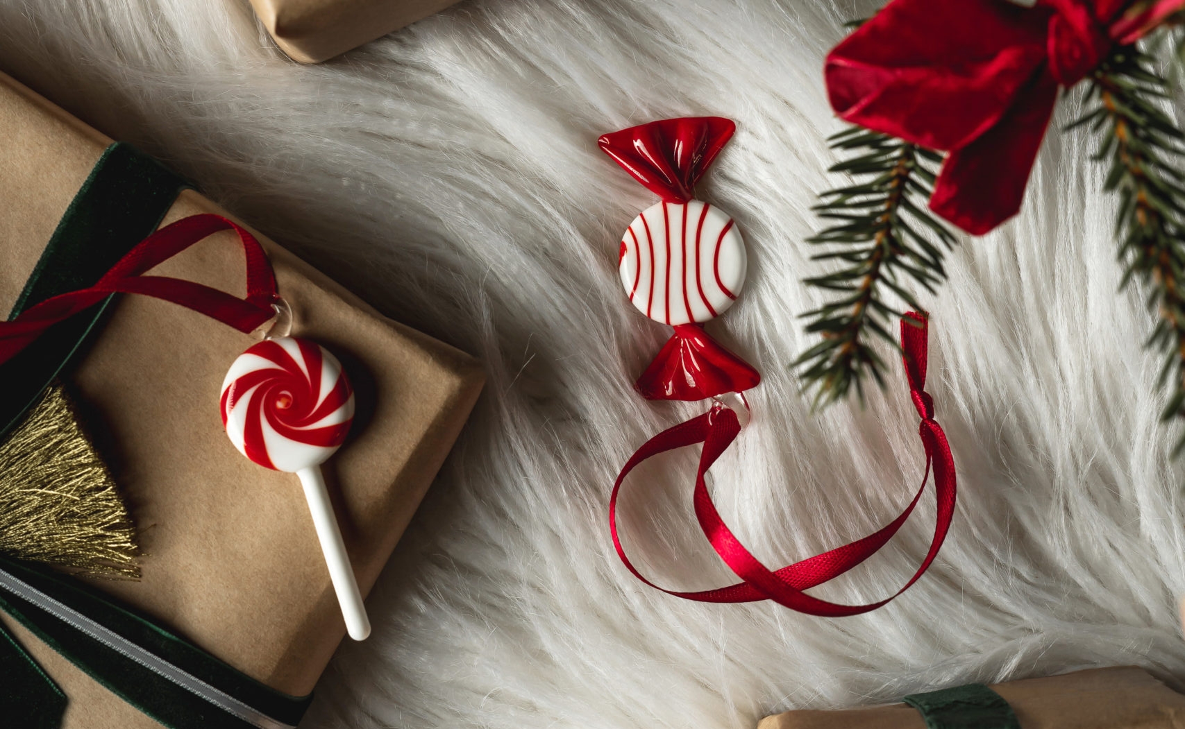 Flat lay of kraft paper gifts with velvet bows, candy ornaments, and evergreen branches on white faux fur.