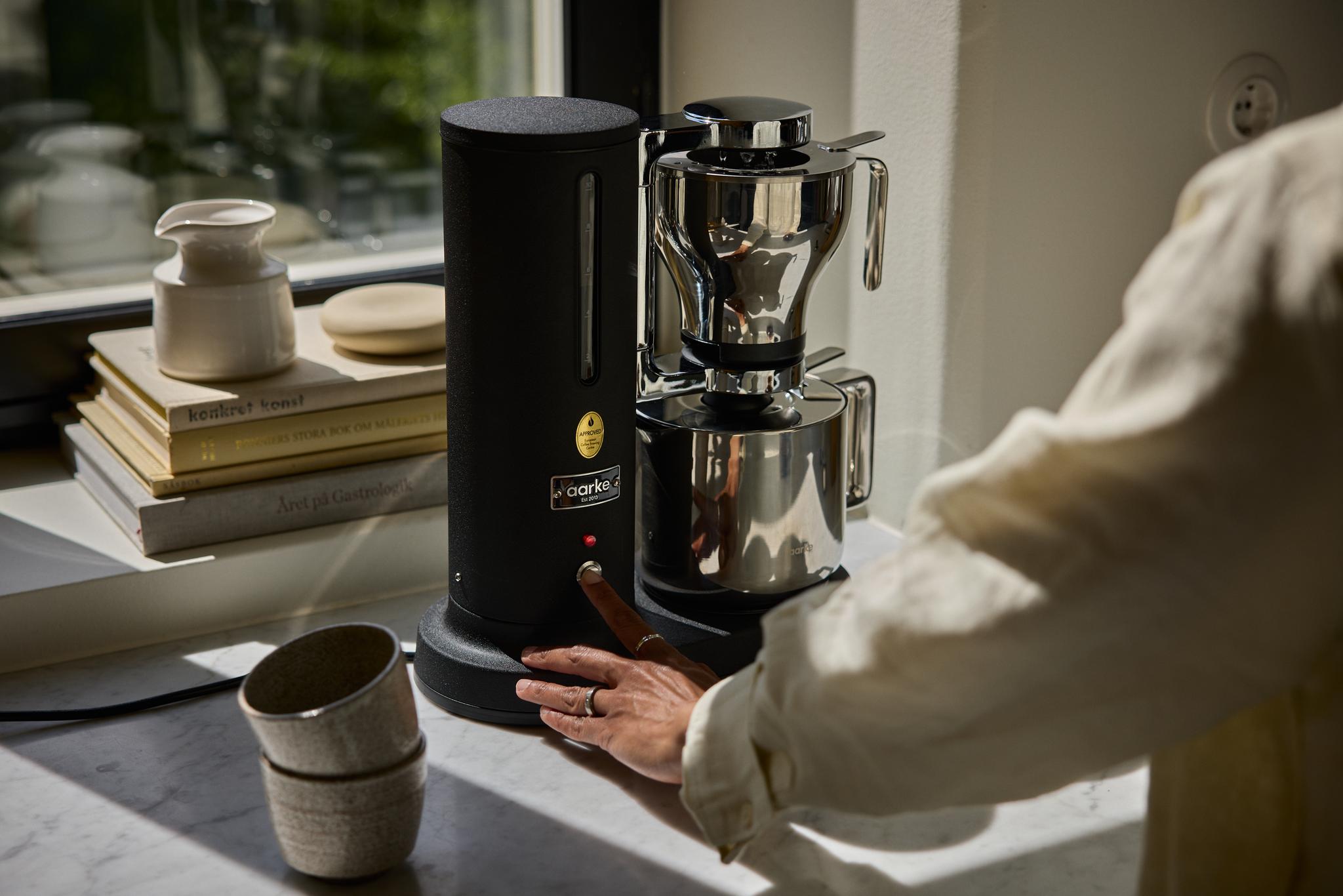 En hand trycker på en knapp på en modern svart och kromad kaffemaskin.