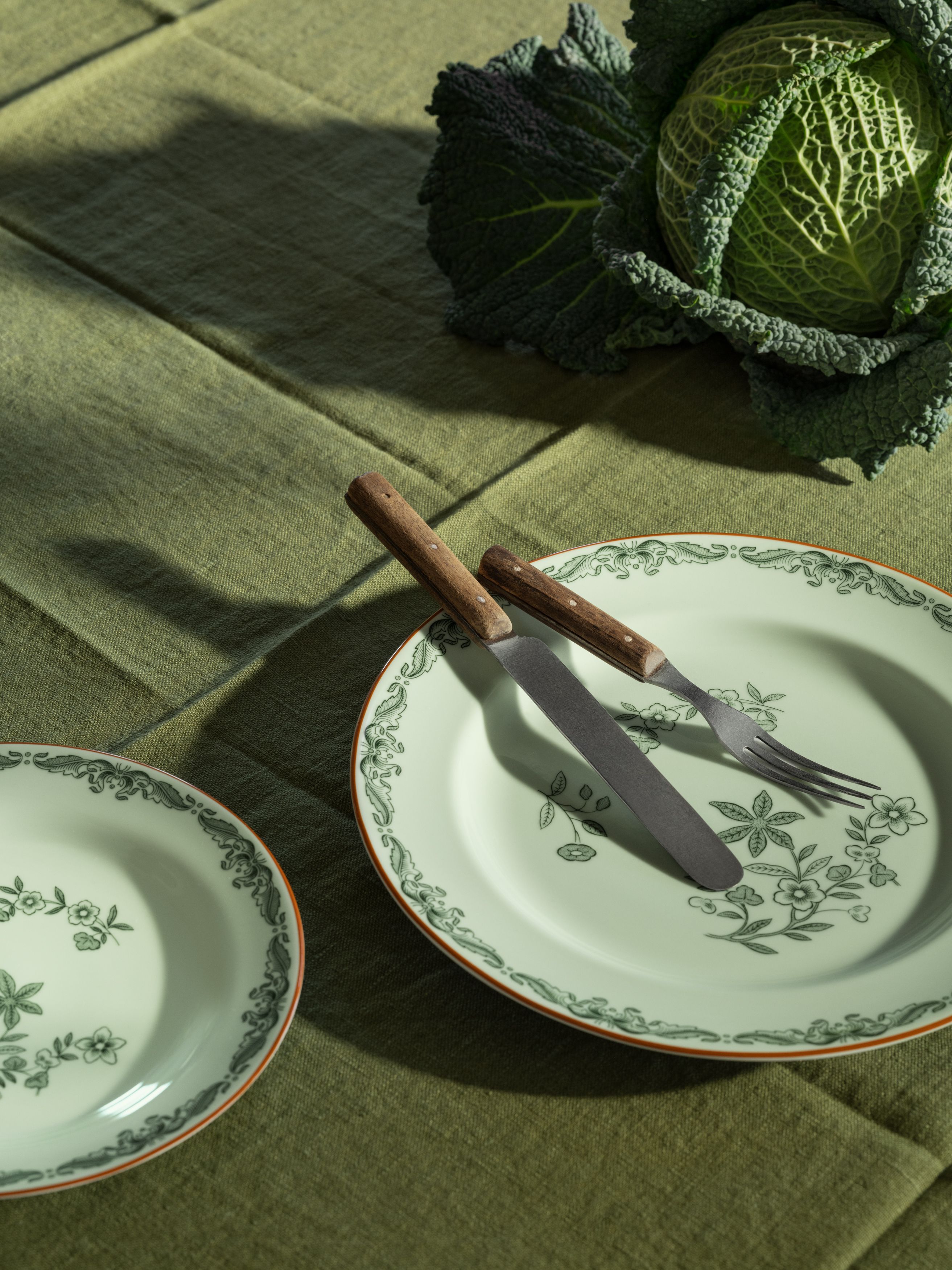 En hel grönkål, två blommiga tallrikar med kniv och gaffel, på en grön duk.
