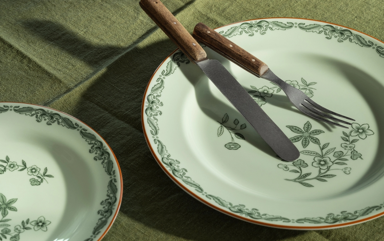 En hel grönkål, två blommiga tallrikar med kniv och gaffel, på en grön duk.