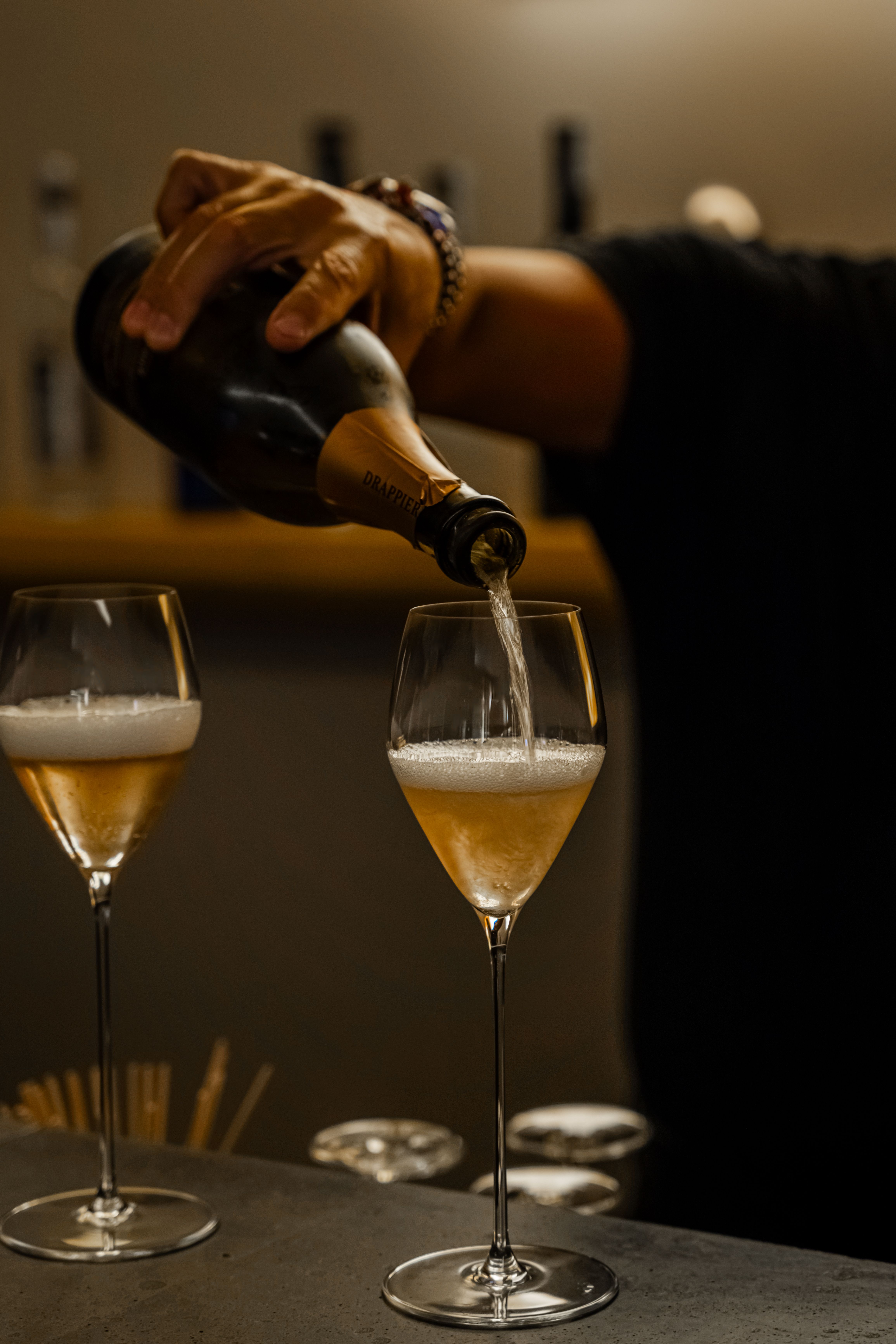 Håndhellende Drappier-champagne i et glass, med et annet glass ved siden av.