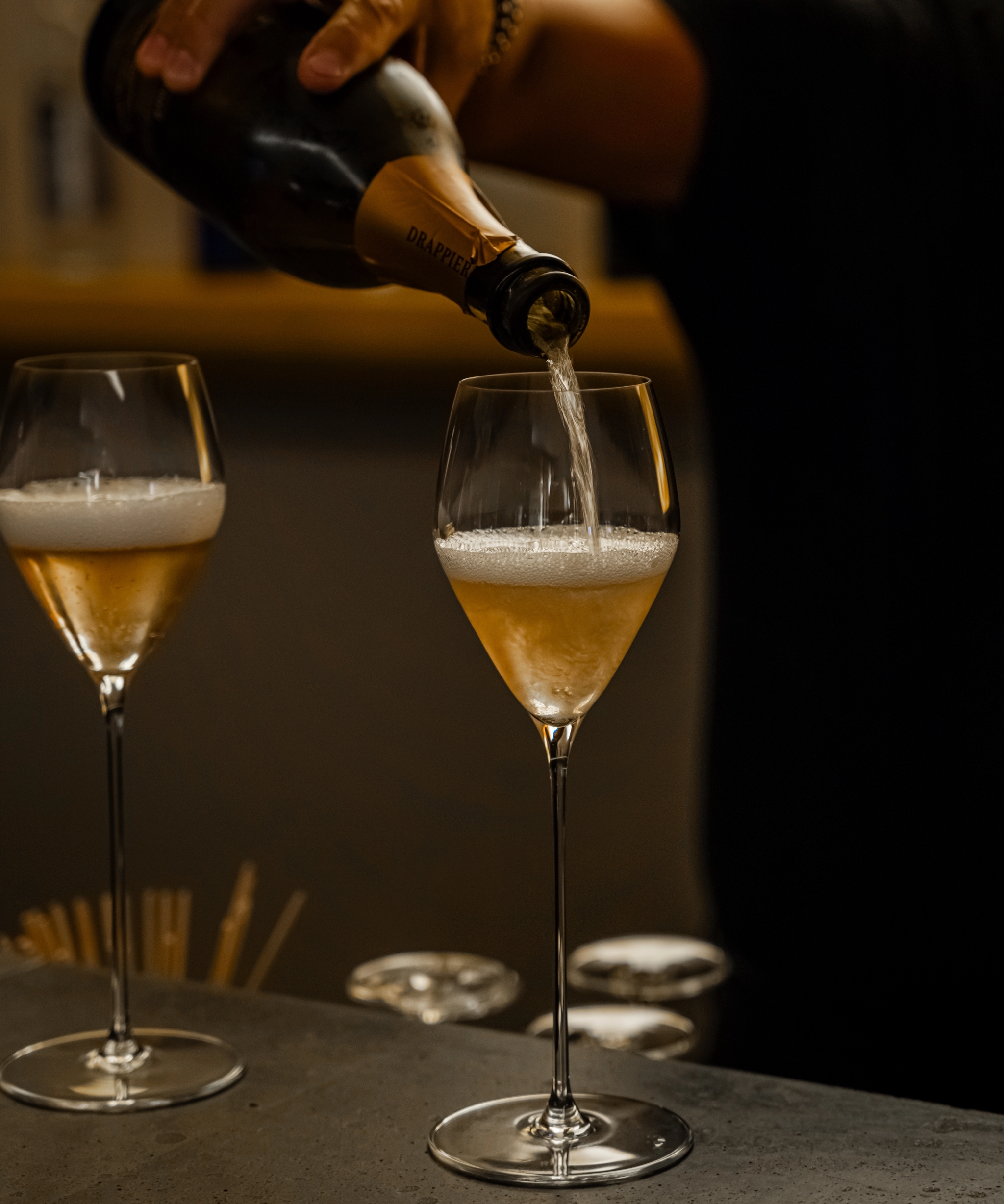 En hand häller Drappier-champagne i ett flöjtglas, bredvid ett annat halvfyllt glas.