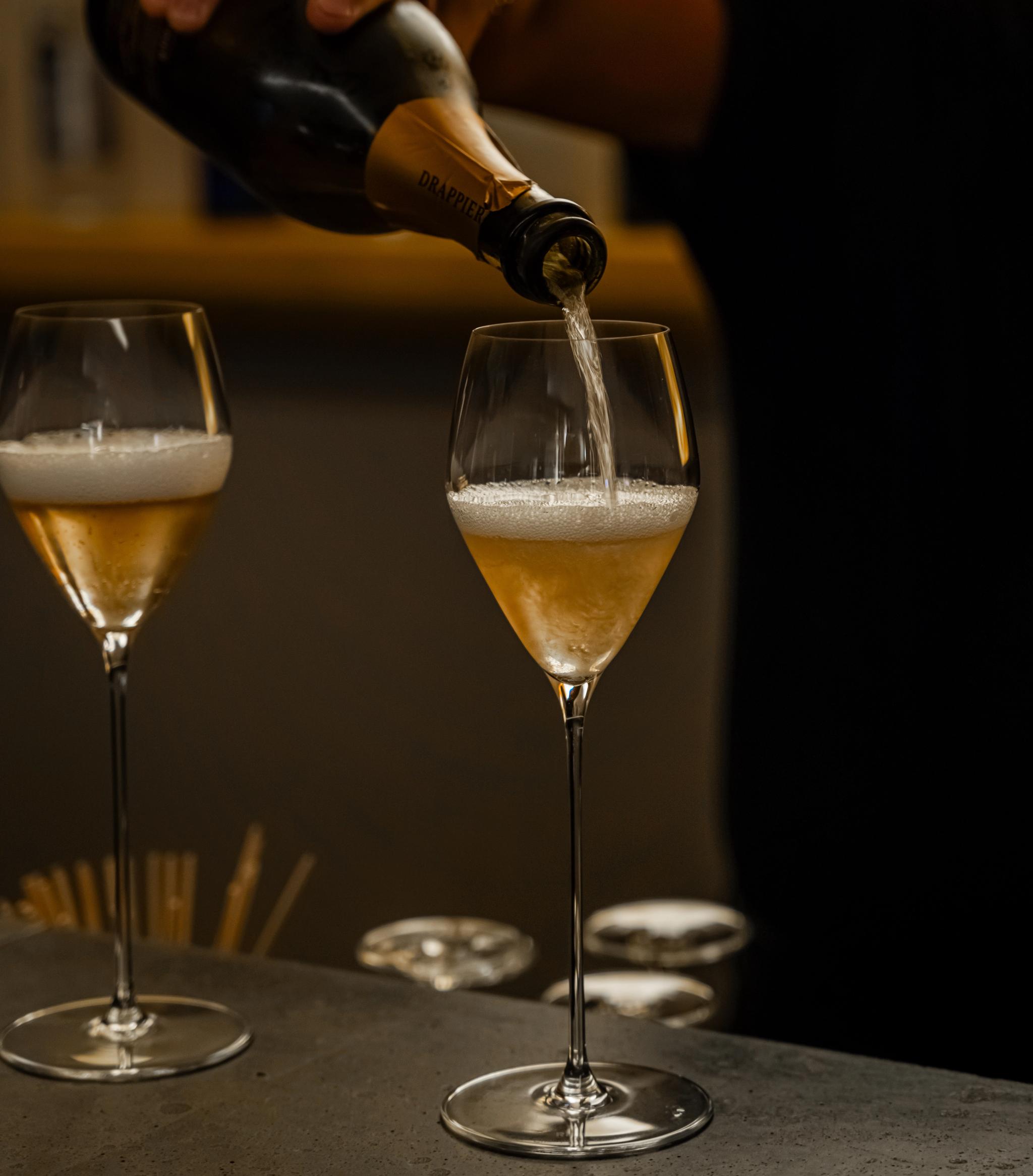 En hand häller Drappier-champagne i ett flöjtglas, bredvid ett annat halvfyllt glas.