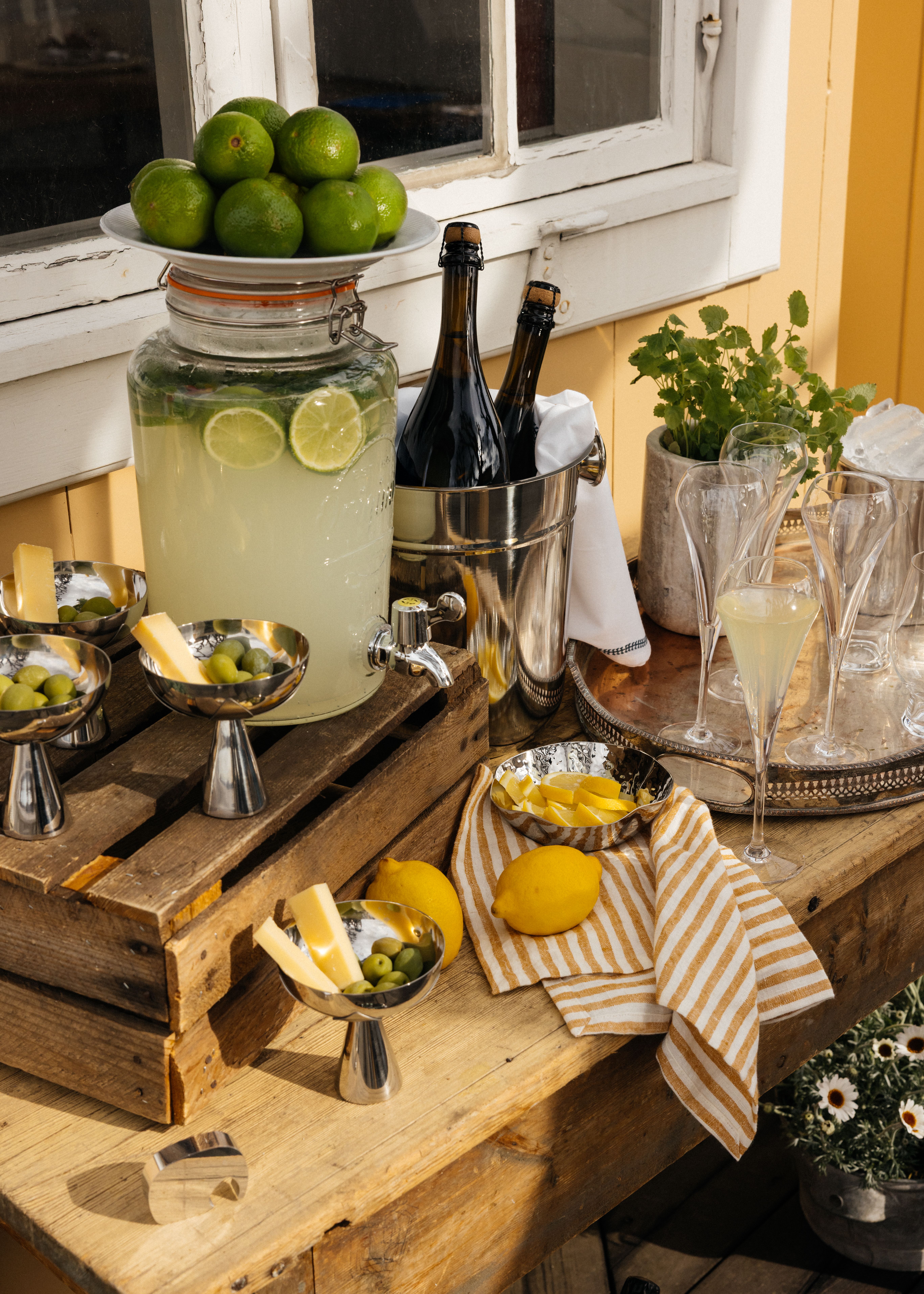 Sommerlig serveringsbord med sitronlimonade, friske sitroner, grønne oliven, ost og musserende vin ute på terrassen.