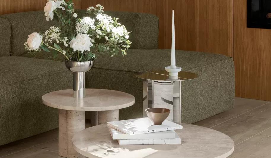Modernt vardagsrum med grön modulsoffa, runda soffbord i sten och blommor mot träpanel.