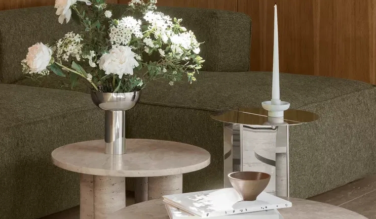 Modernt vardagsrum med grön modulsoffa, runda soffbord i sten och träpaneler på väggarna.