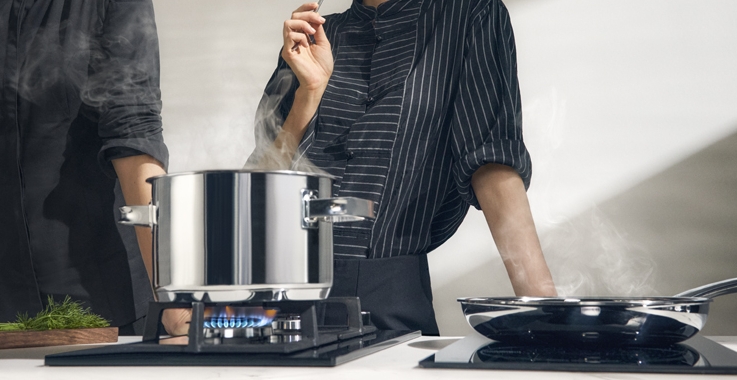 Två kockar lagar mat med en ångande gryta på en gasbrännare och en stekpanna på en induktionshäll.