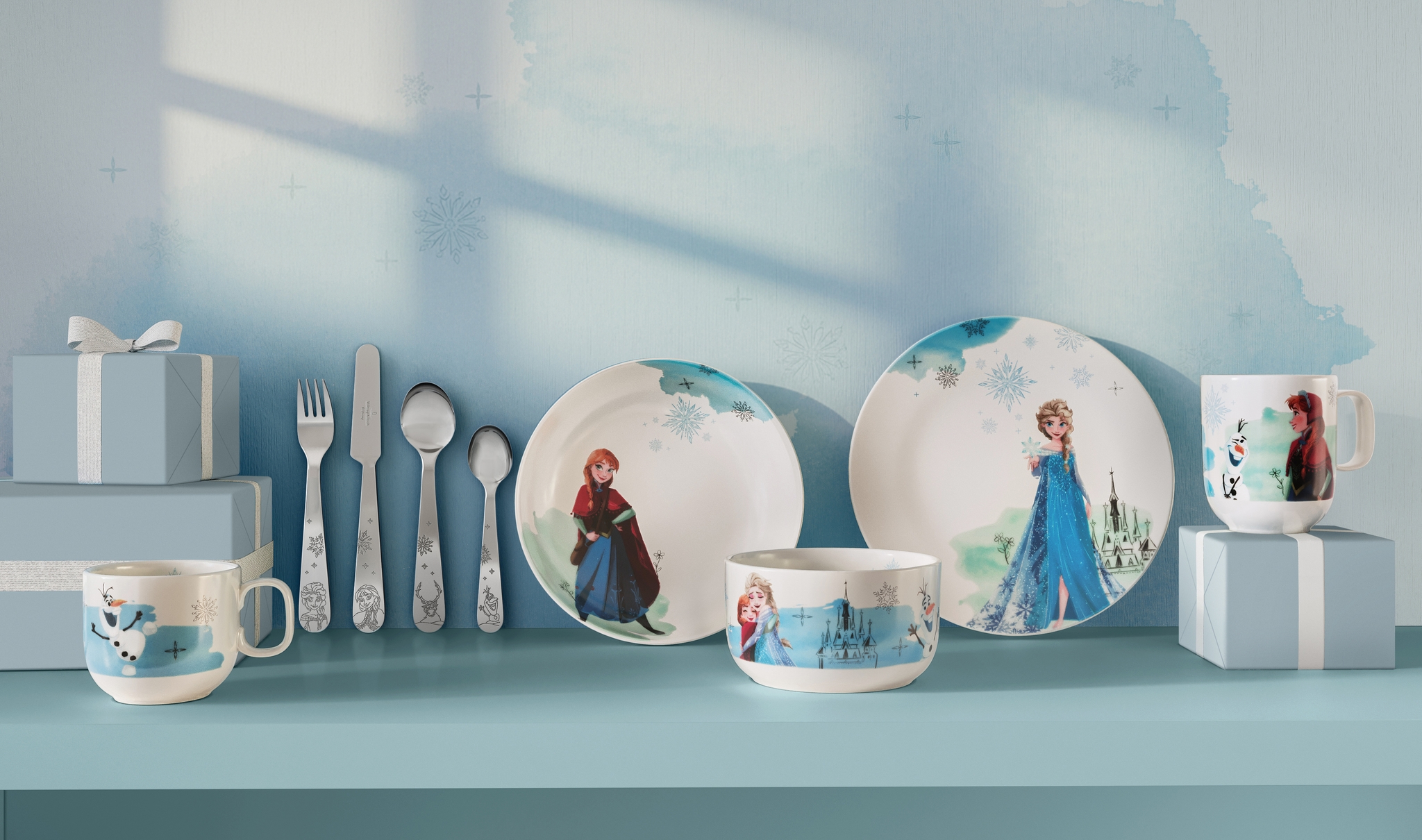 Disney Frost-servise med tallerkener, kopper og bestikk med Anna, Elsa og Olaf på en lyseblå hylle.