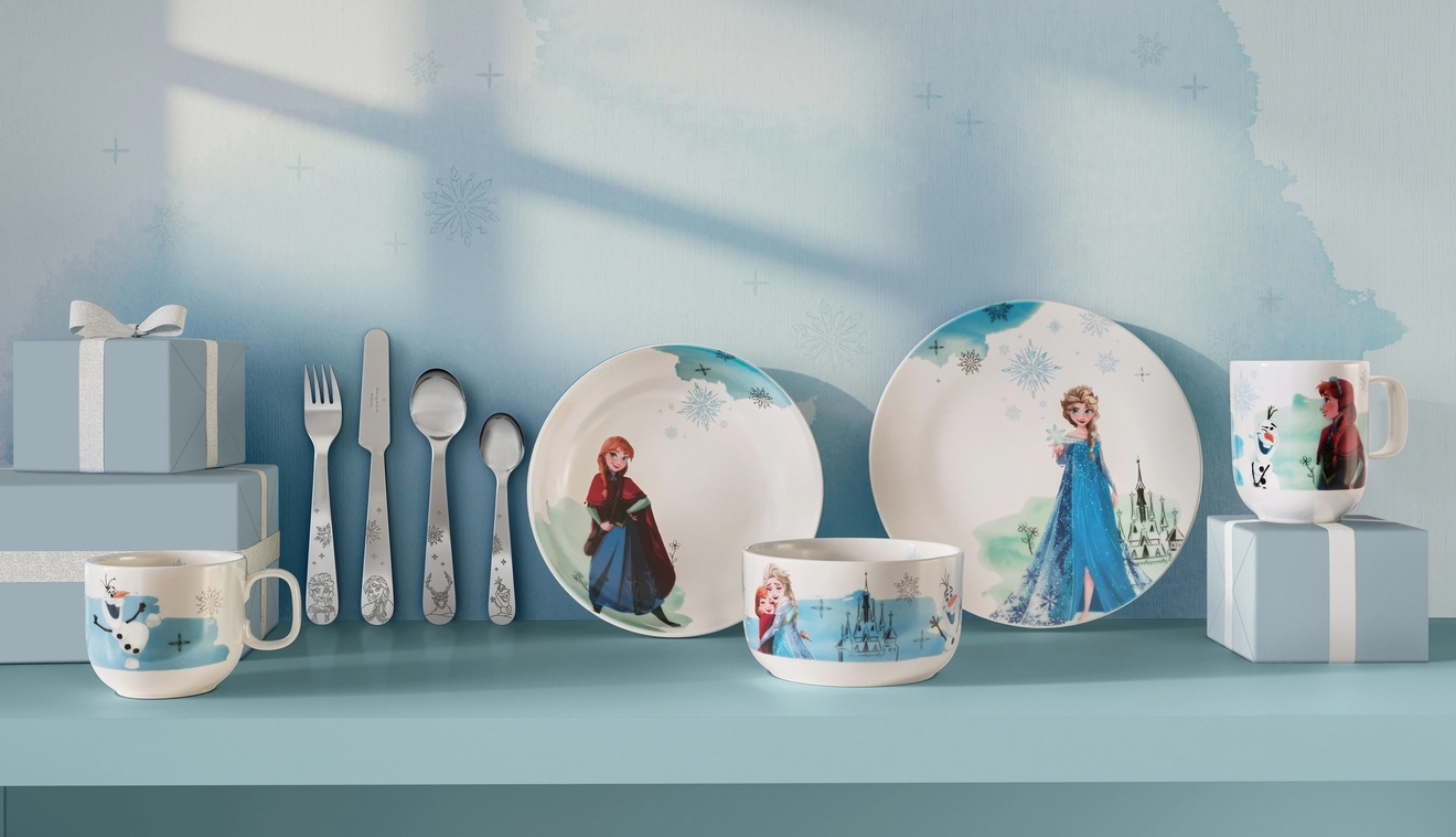 Disney Frost-servis med tallrikar, muggar och bestick med motiv av Elsa, Anna och Olaf uppställda på ett blått bord.