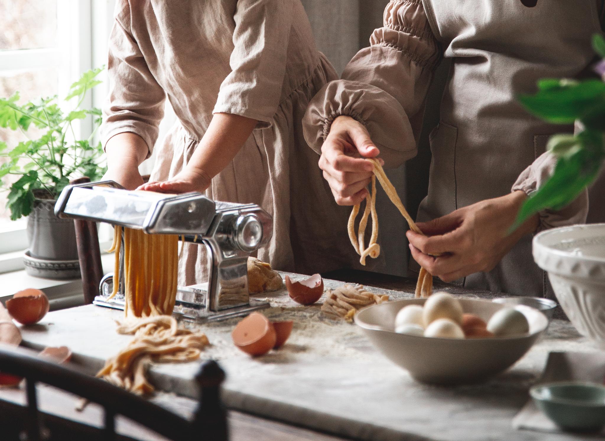 Ett barn och en vuxen gör färsk pasta med hjälp av en pastamaskin på en köksbänk.