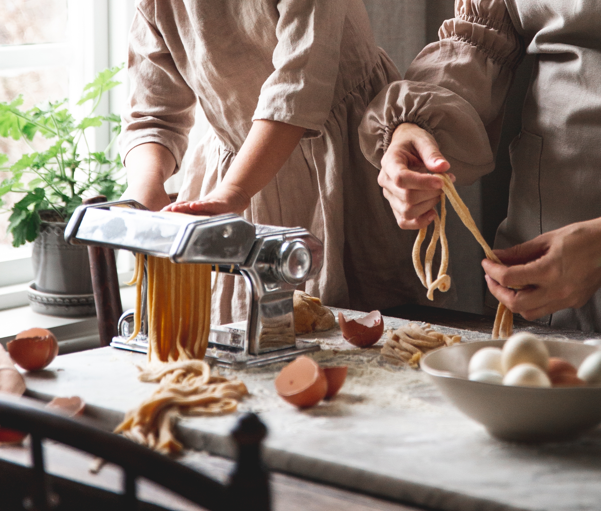 Ett barn och en vuxen gör färsk pasta med hjälp av en pastamaskin på en köksbänk.