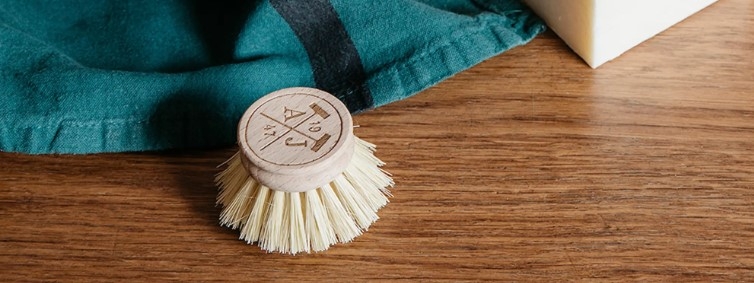 Borste, diskborsthuvud i trä liggandes på träbord med blå kökshandduk i bakgrunden