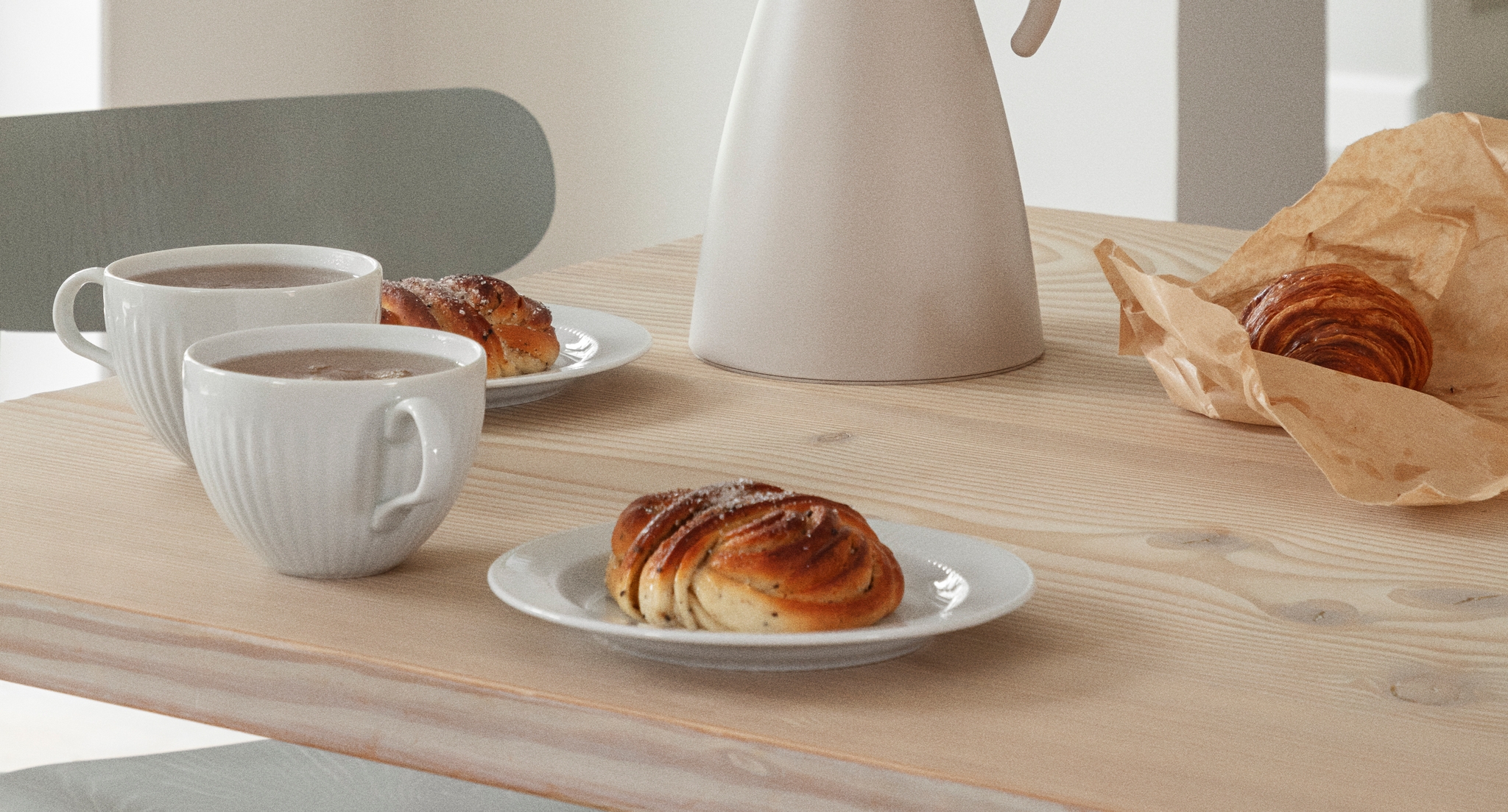Vaalealle puupöydälle katettu kahvihetki, jossa on valkoinen kannu, kahvikuppeja, korvapuusteja ja croissant.