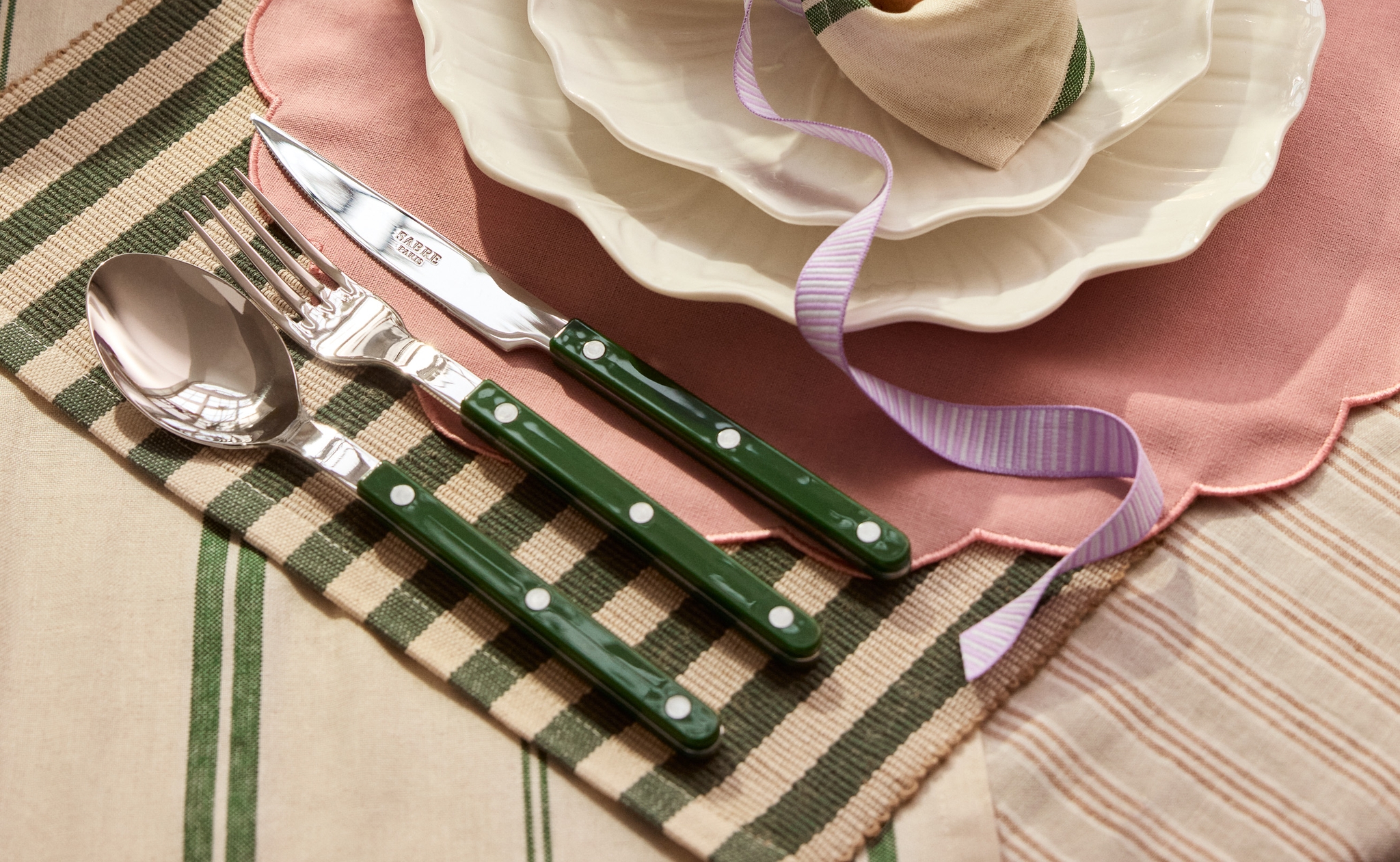 Keväinen kattaus, jossa on vaaleanpunainen aaltoreunainen pöytätabletti, valkoiset lautaset, pupunkorvien muotoon sidottu servetti, jonka sisällä on muna ja mimosankukkia, sekä vihreävartiset aterimet